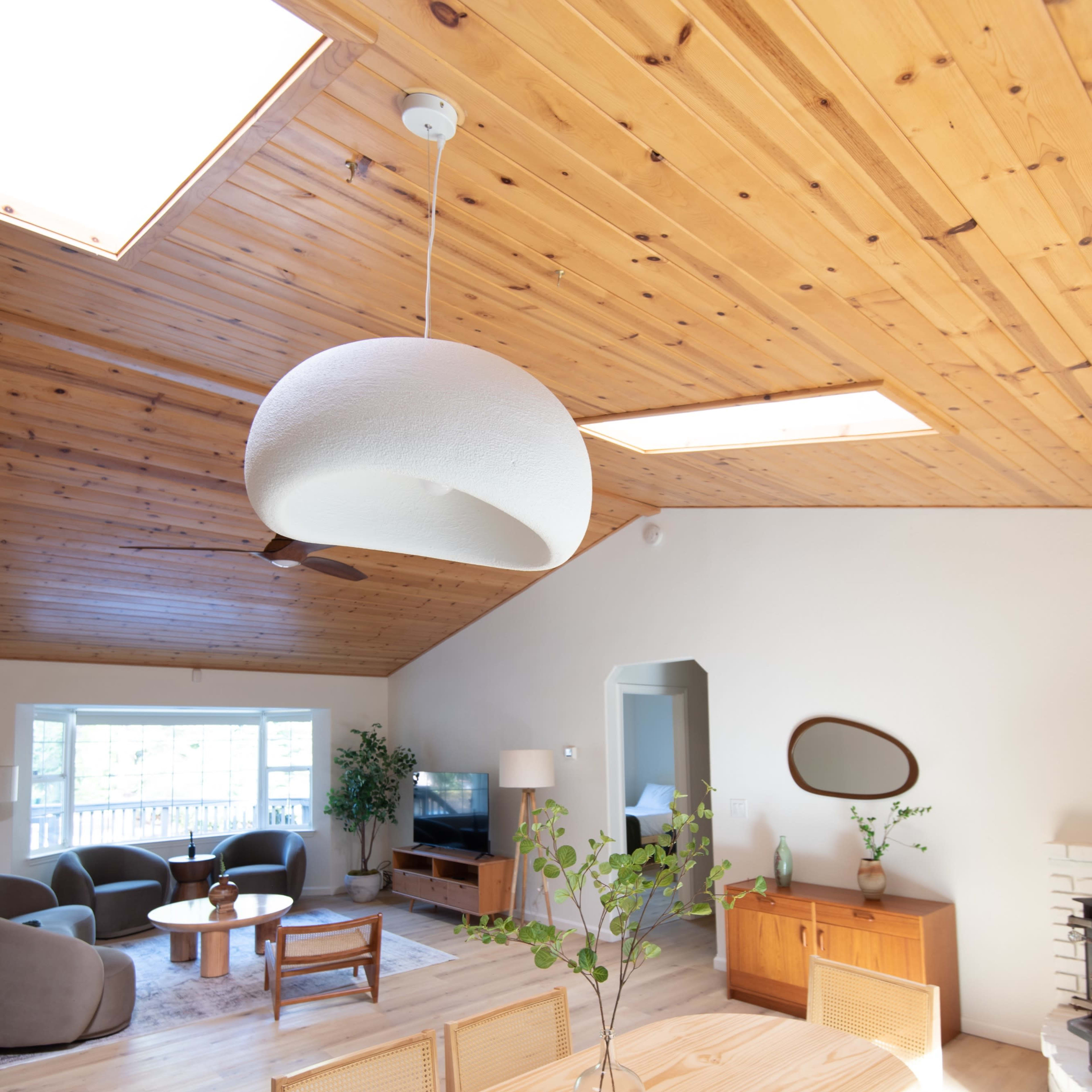 A modern, open-concept living space featuring a wooden ceiling, large windows, a dining table, and various seating arrangements.