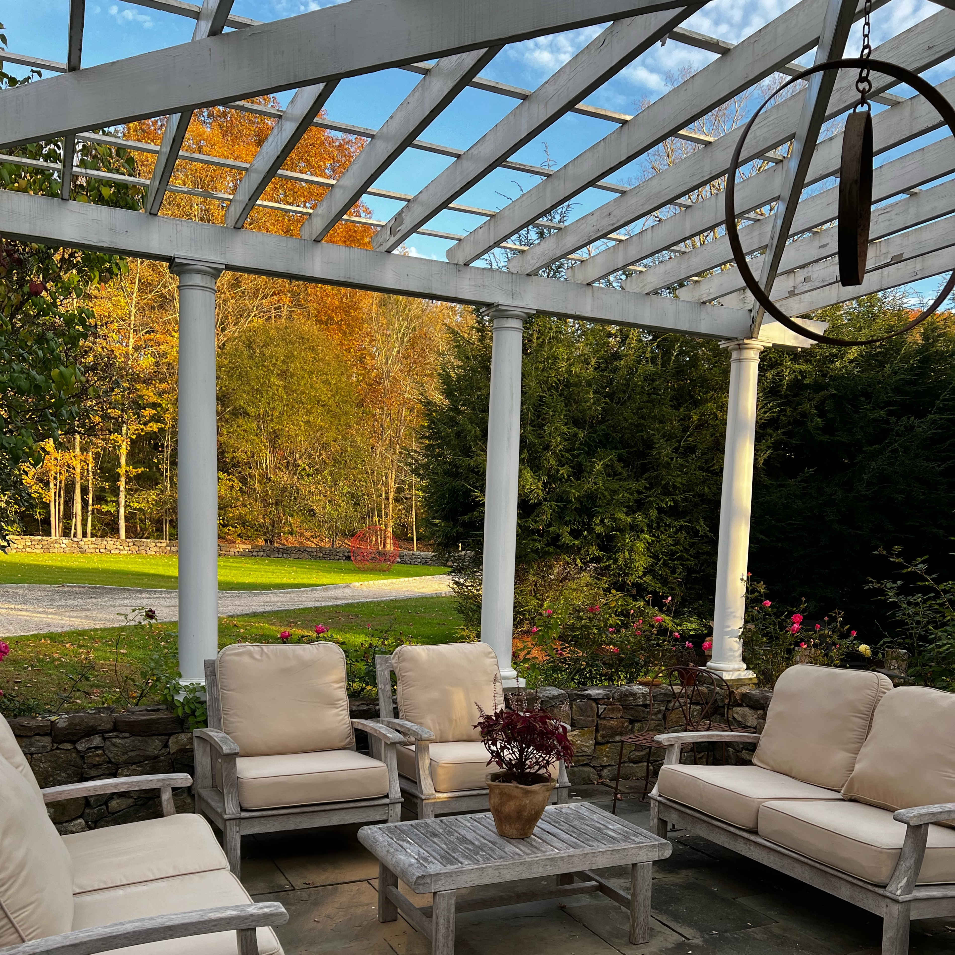 A patio area features four beige chairs and a matching table surrounded by a stone wall and greenery.