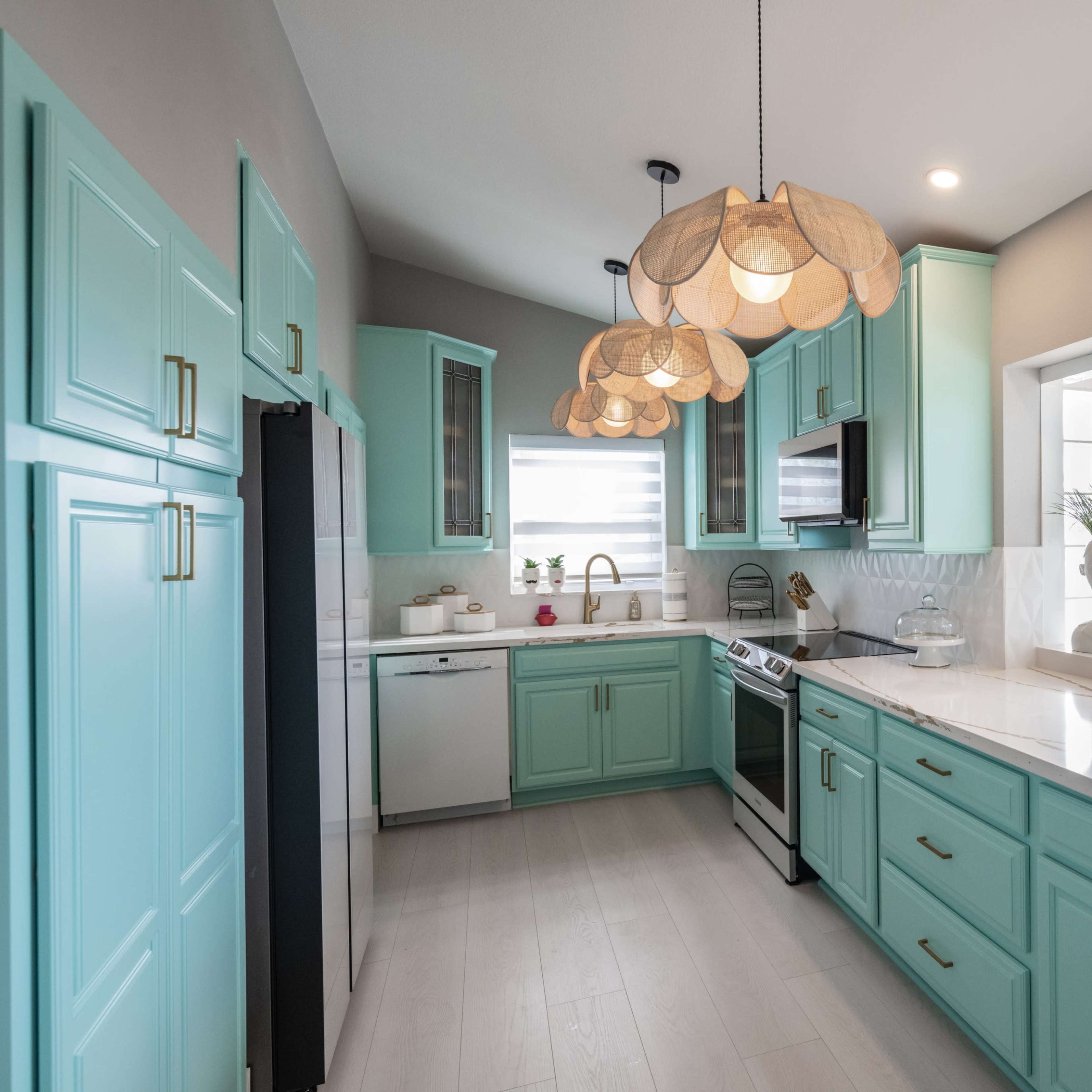 A modern kitchen featuring light blue cabinetry, a marble countertop, and pendant lighting above the workspace.