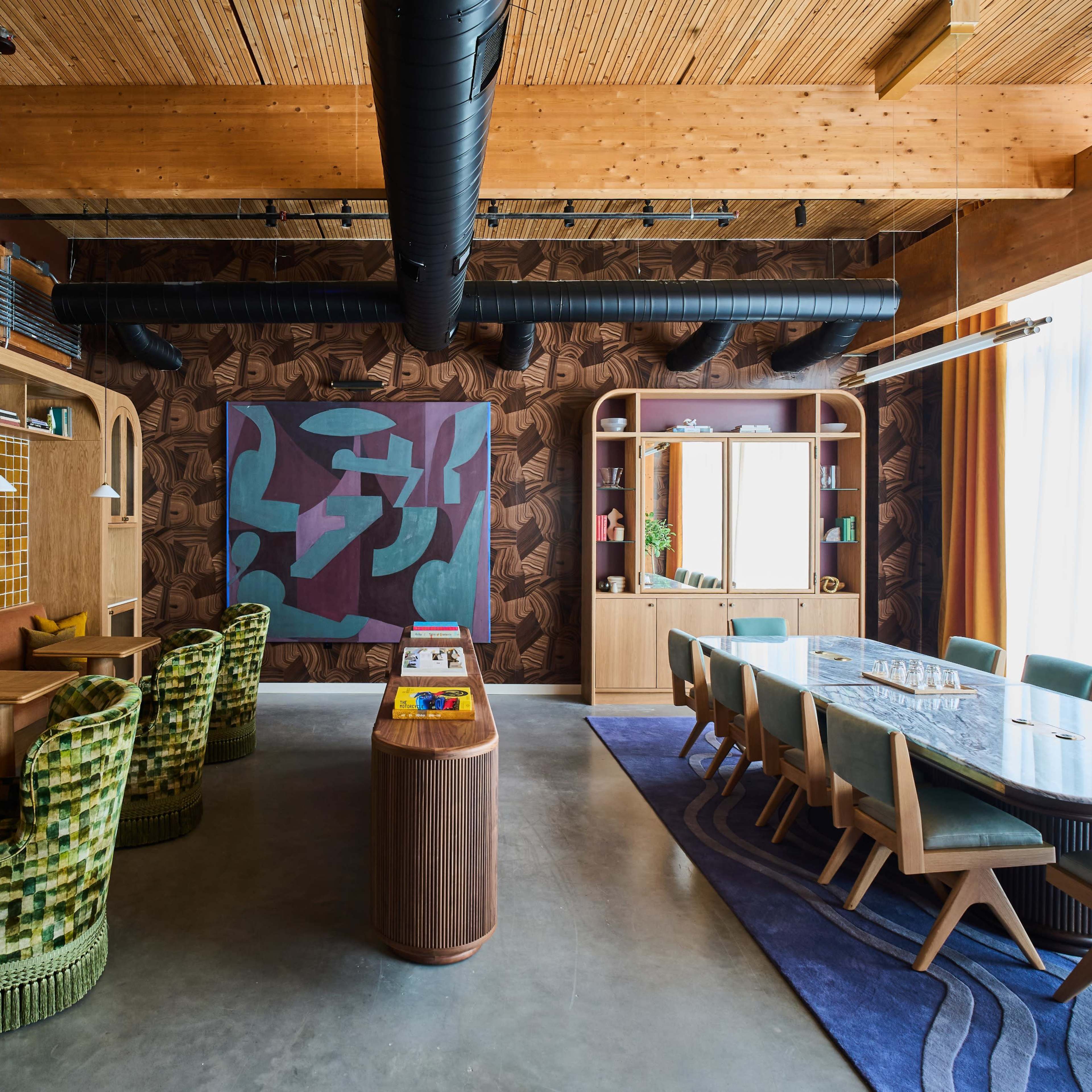 A modern dining area with a combination of vibrant wall decorations, a long wooden table surrounded by chairs, and a cozy seating nook with patterned green chairs.