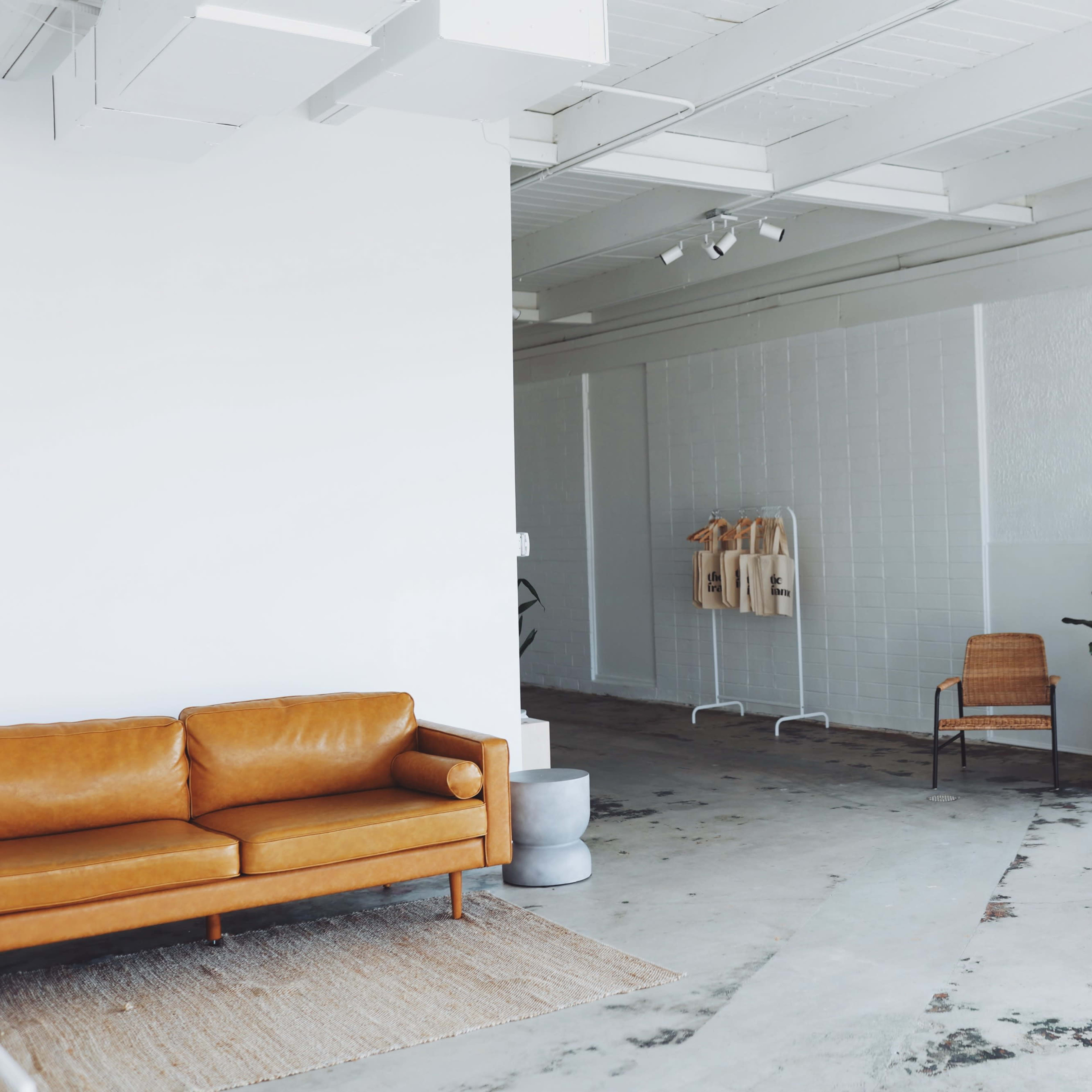 A spacious interior with a brown leather sofa, a large mirror, a rattan chair, and several potted plants.