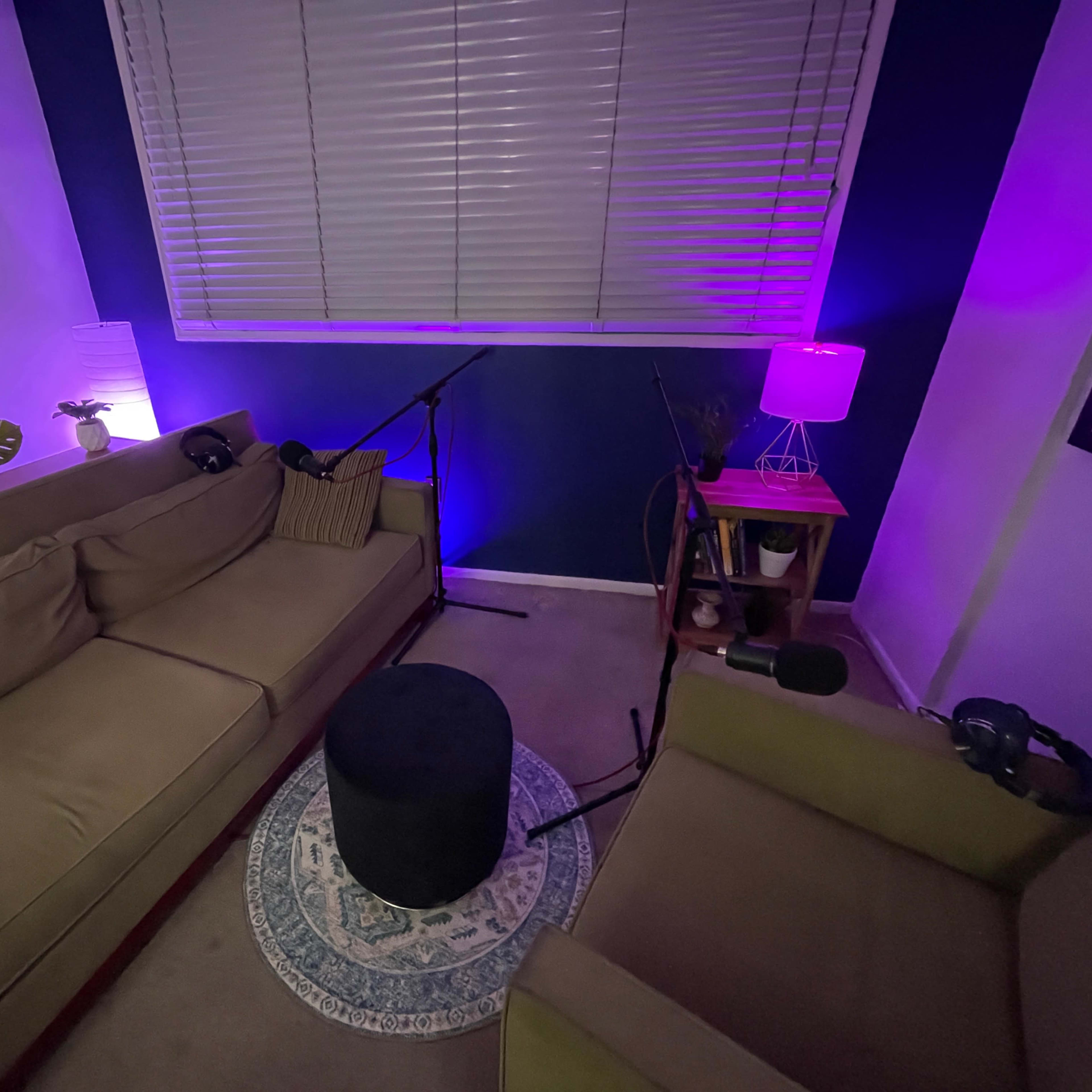A small recording studio is set up with two couches, microphones, and ambient lighting.
