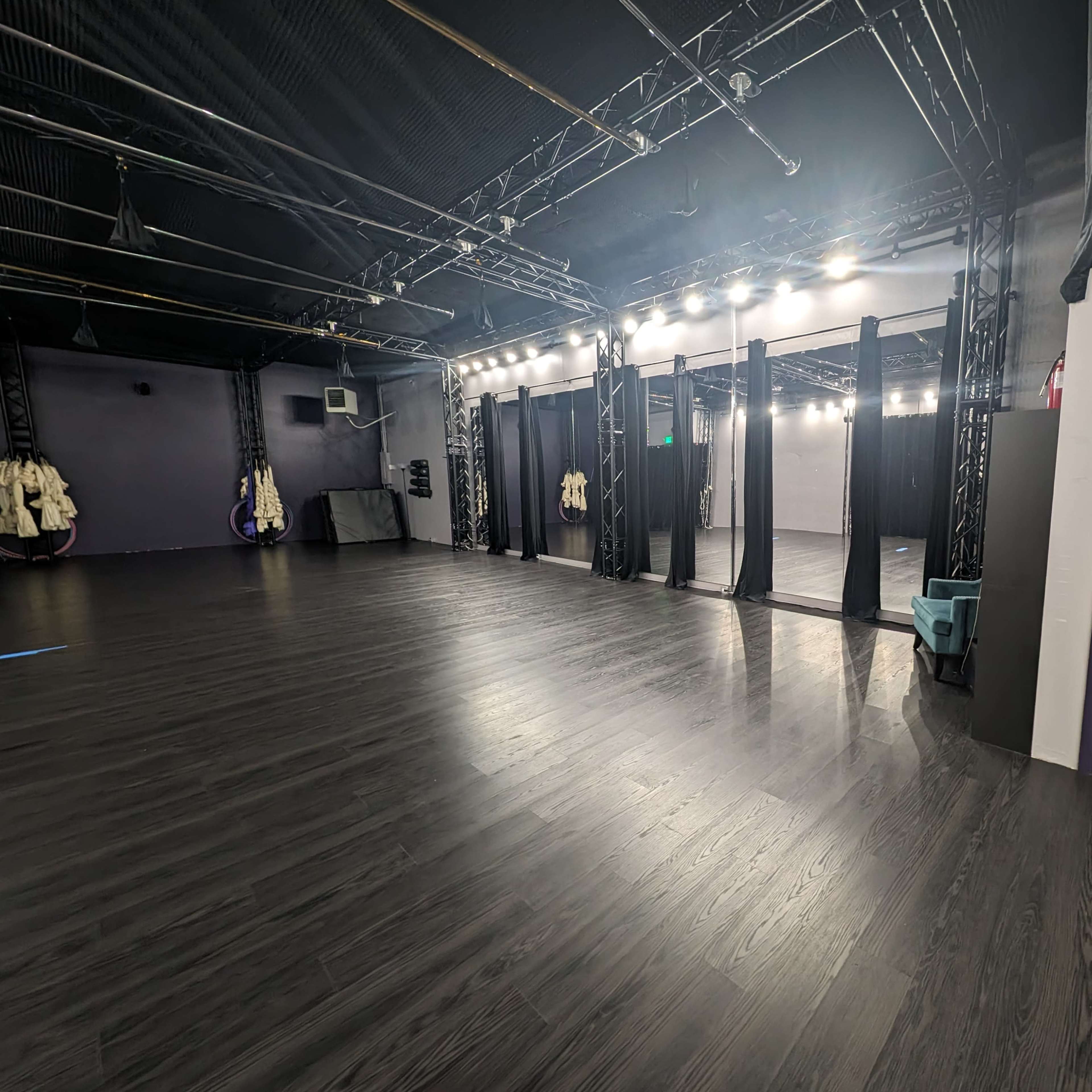 An empty dance studio with polished wood floors, brightly lit mirrors, and black curtains separating performance areas.