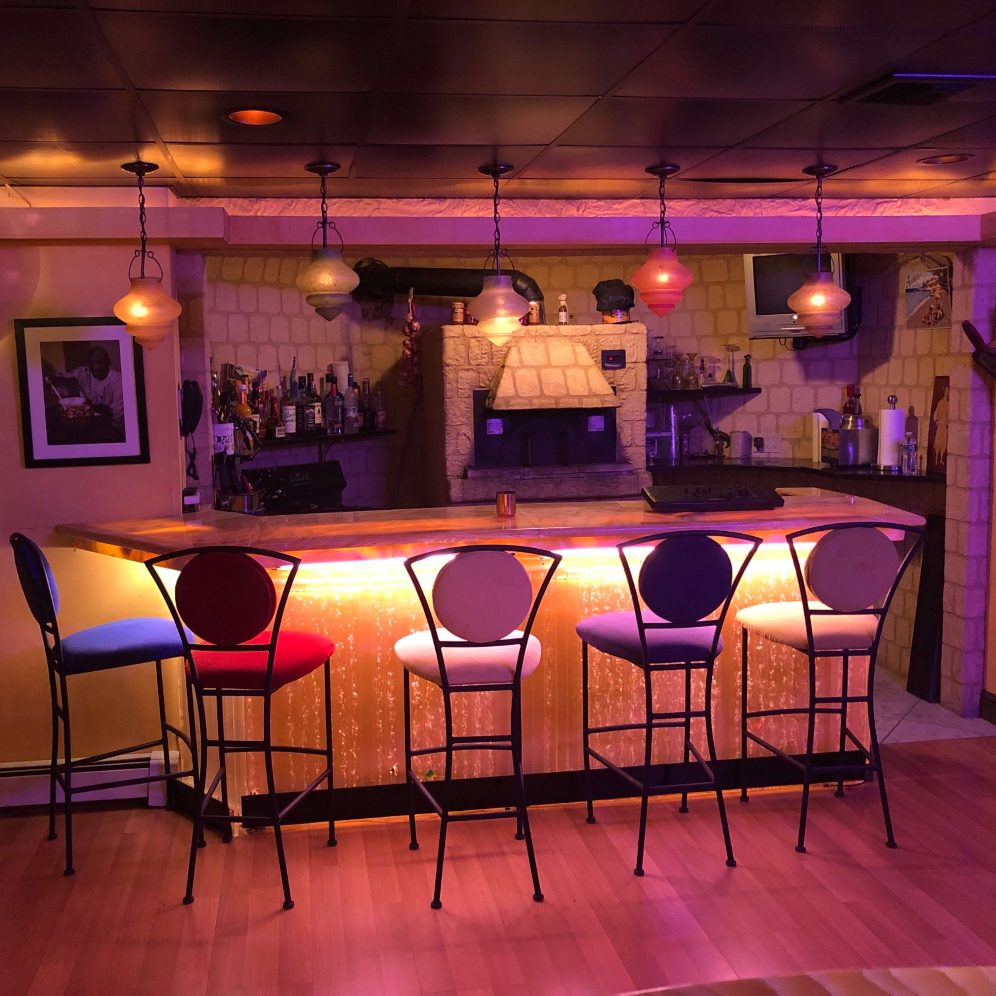 A well-lit bar with colorful, illuminated stools stands against a textured stone wall in a cozy room.