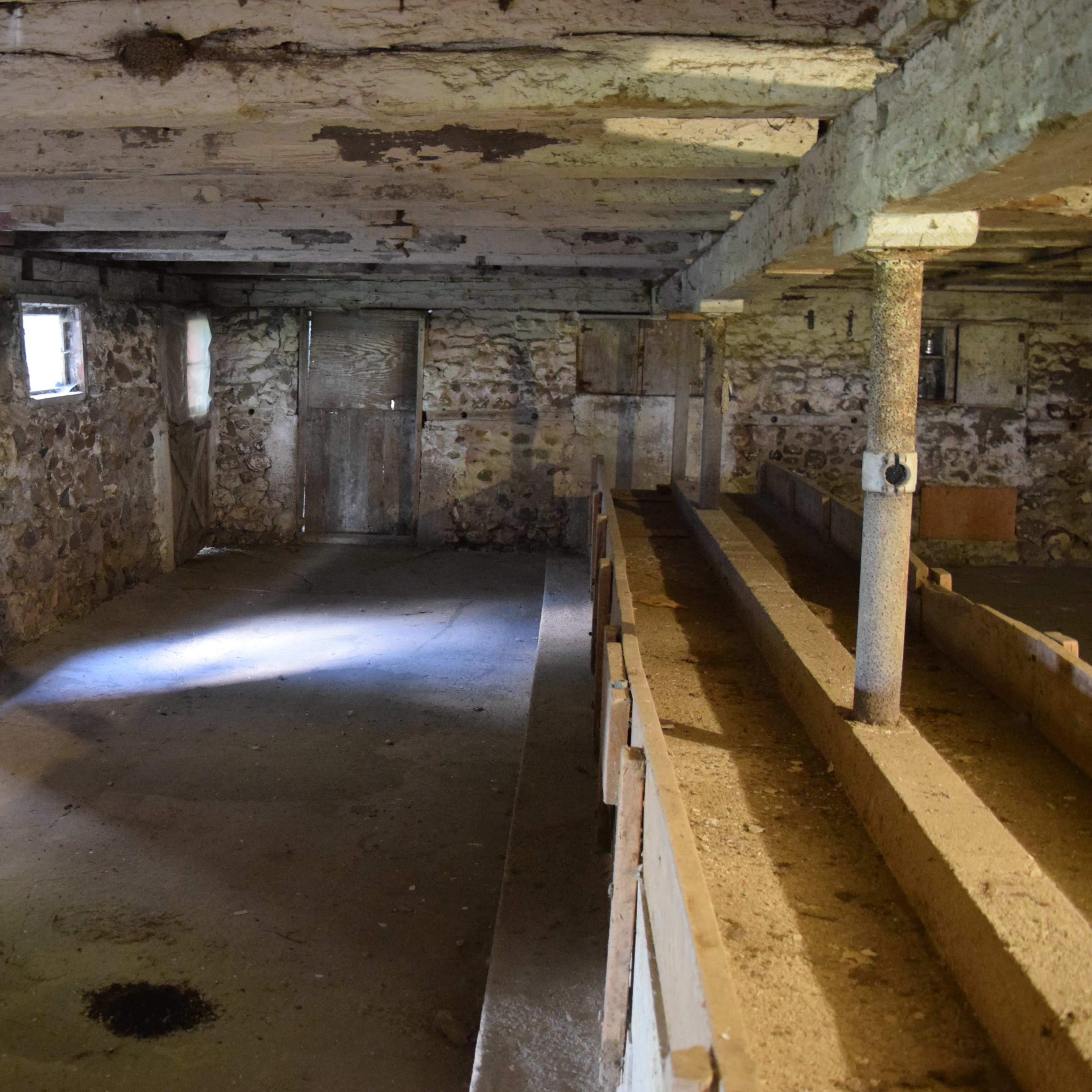 A dimly lit, empty interior of a rustic stone building with wooden beams and a dirt floor.