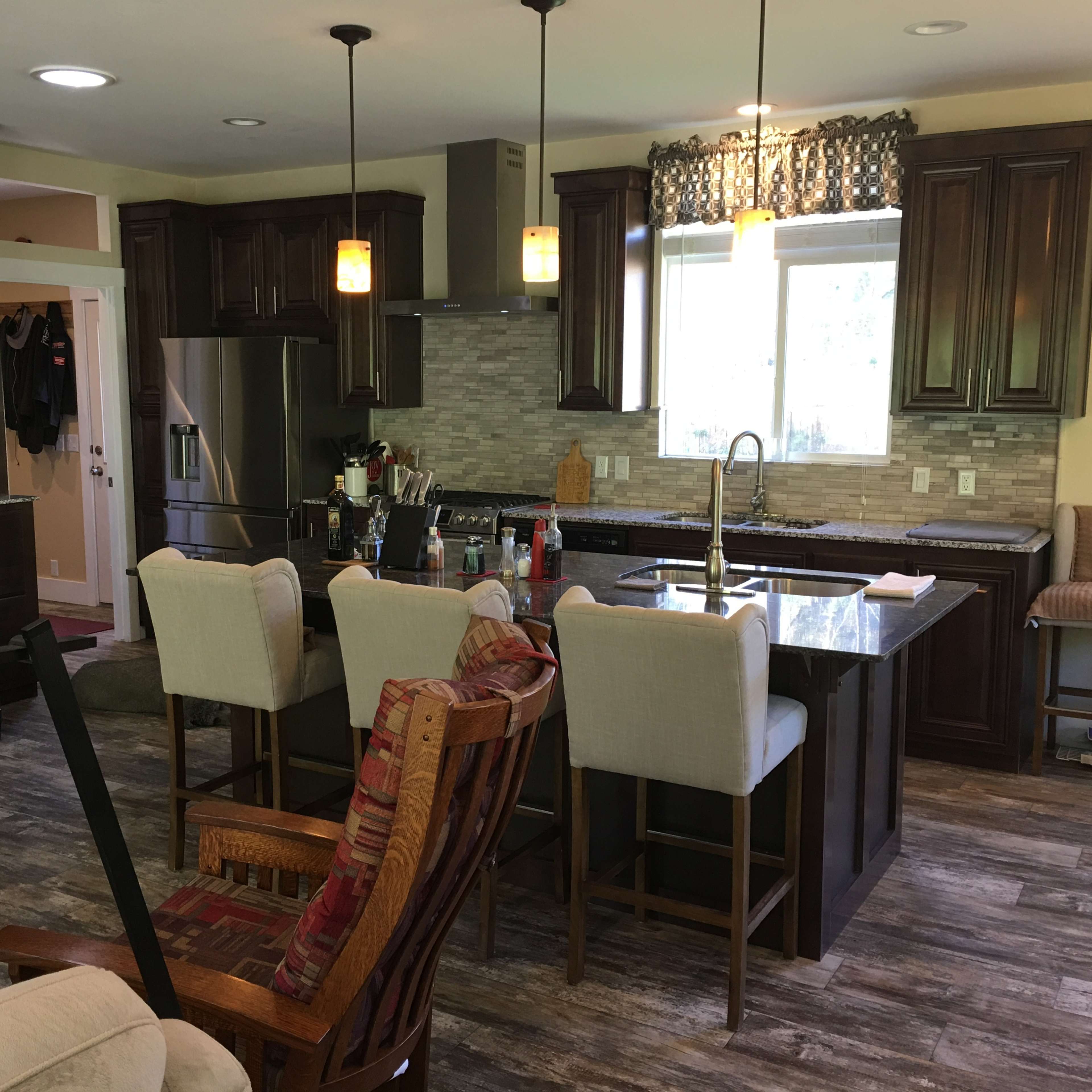A modern kitchen with dark wooden cabinets, a central island with seating for four, and stainless steel appliances.