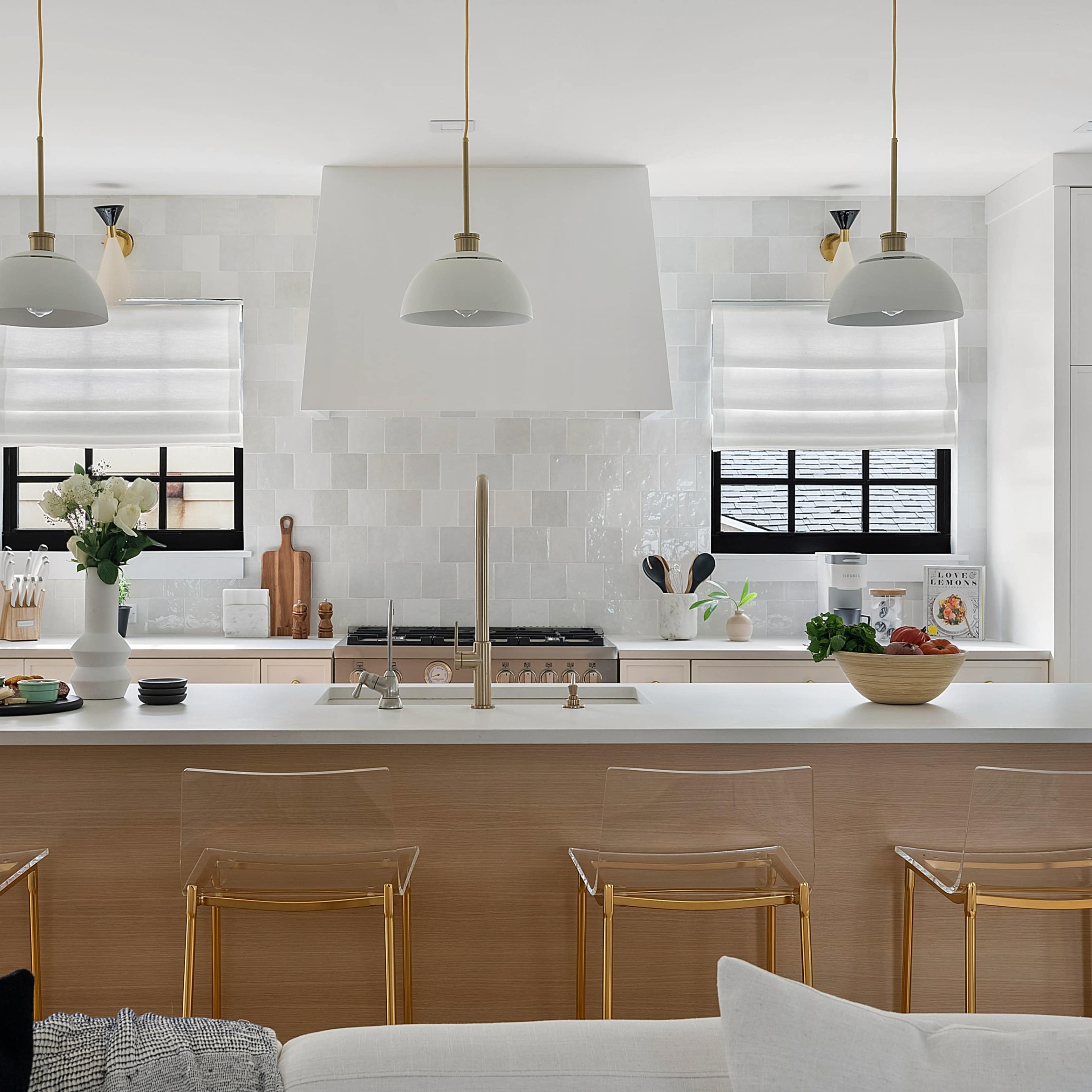 The kitchen features a large island with transparent stools, white cabinets, and a tiled backsplash, illuminated by pendant lights.