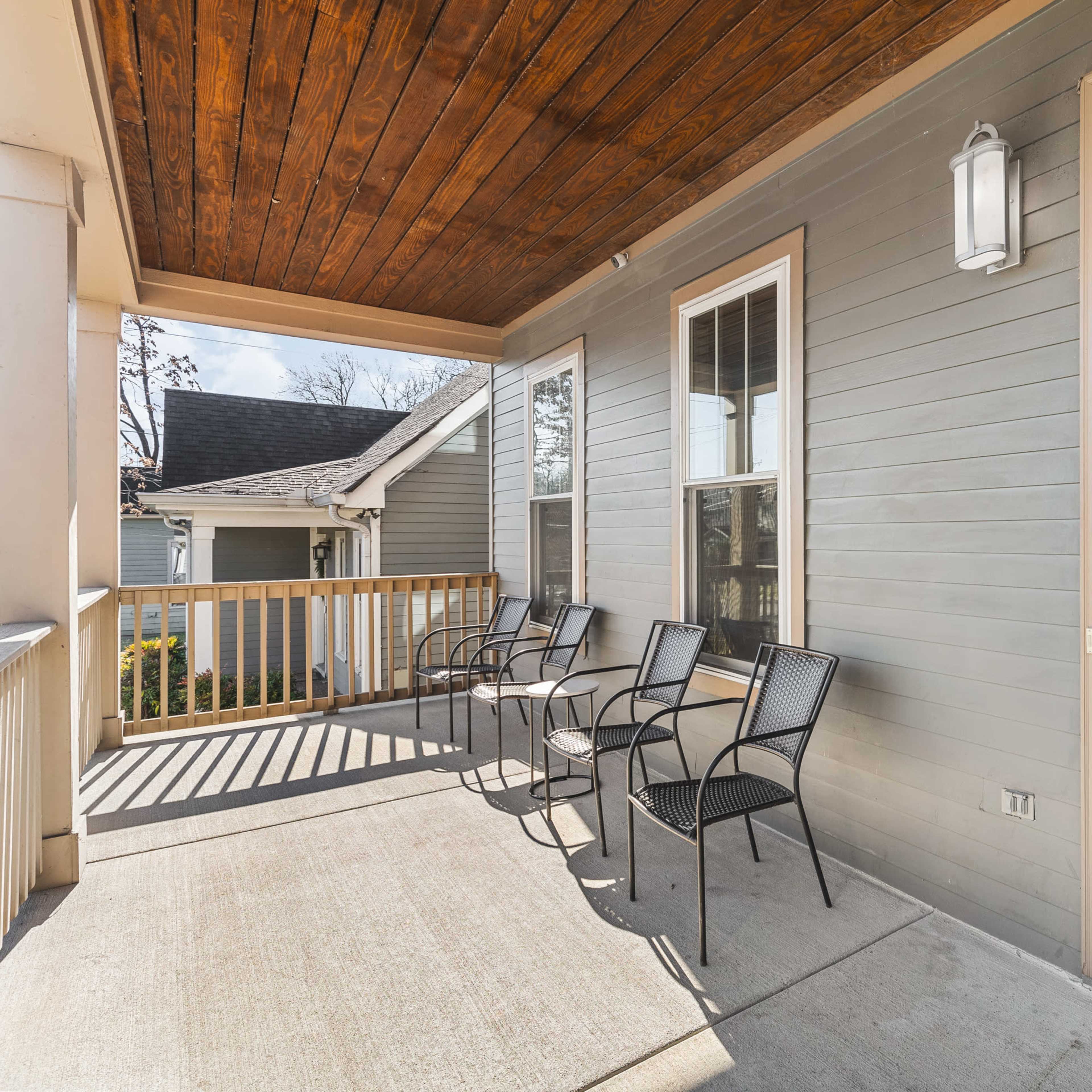 A covered porch features four black metal chairs and leads to an interior space with visible hardwood flooring and light-colored walls.