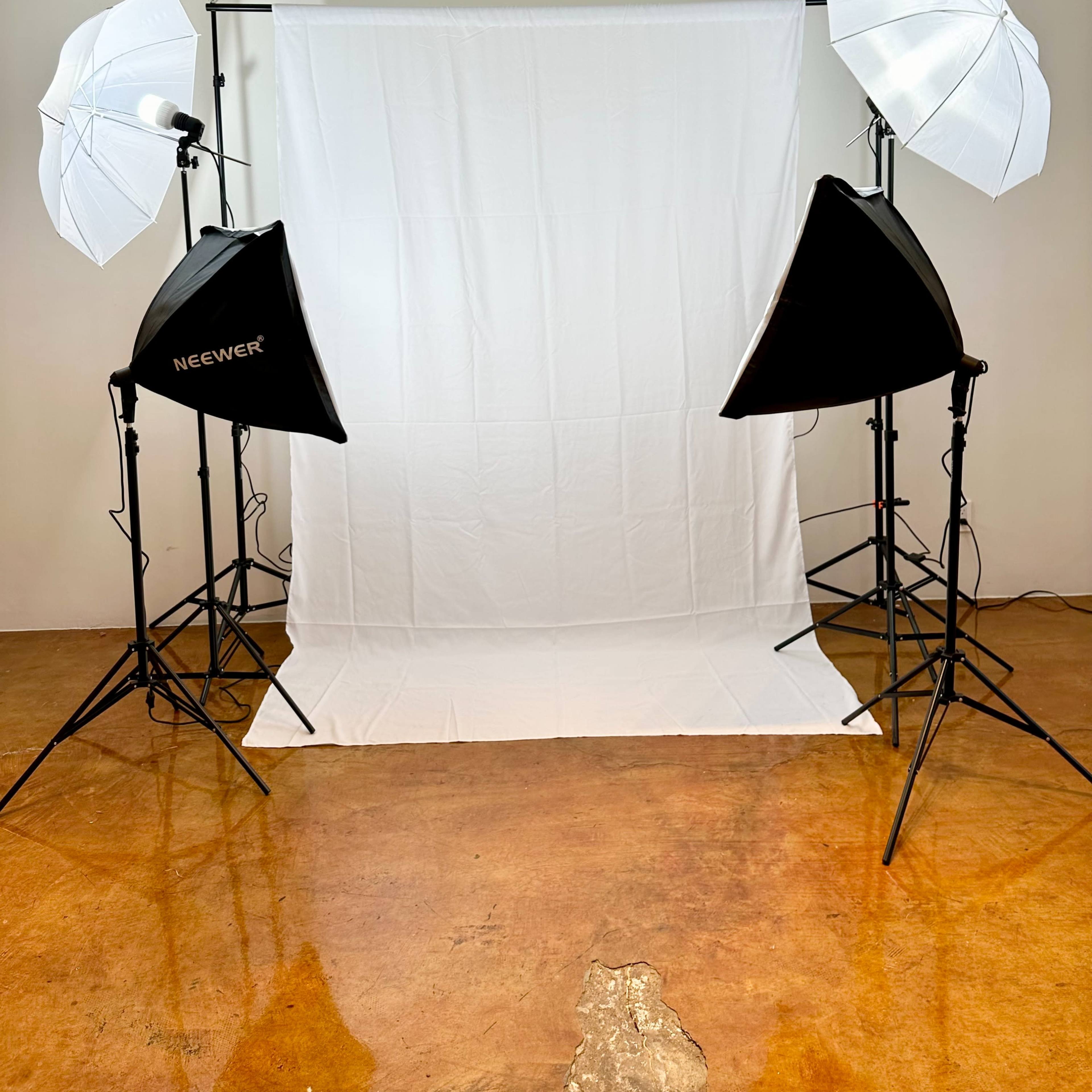 A photography setup with two softbox lights and a white backdrop on a stand in a studio space.