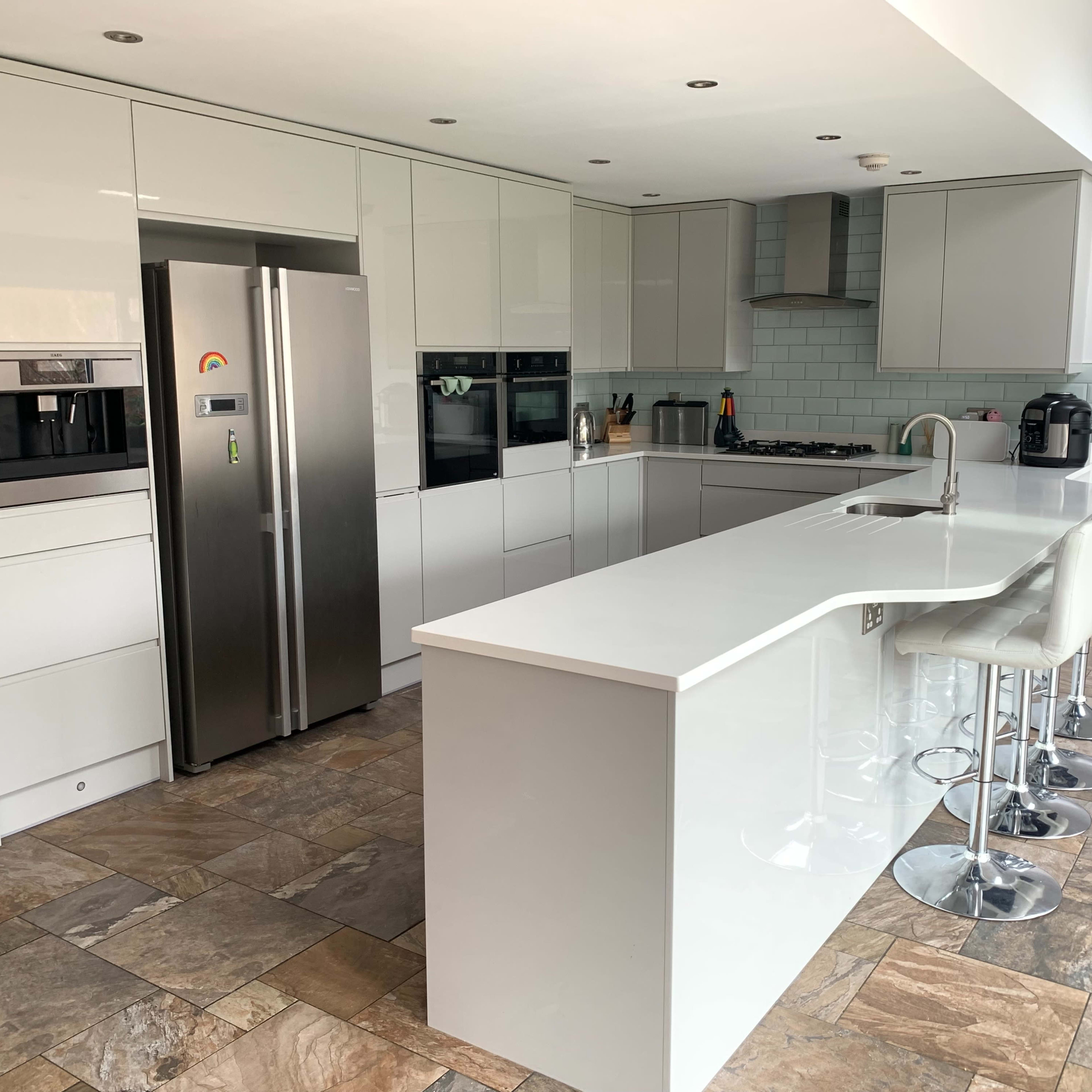 A modern kitchen features gray cabinetry, stainless steel appliances, a large island with bar stools, and a tiled floor.