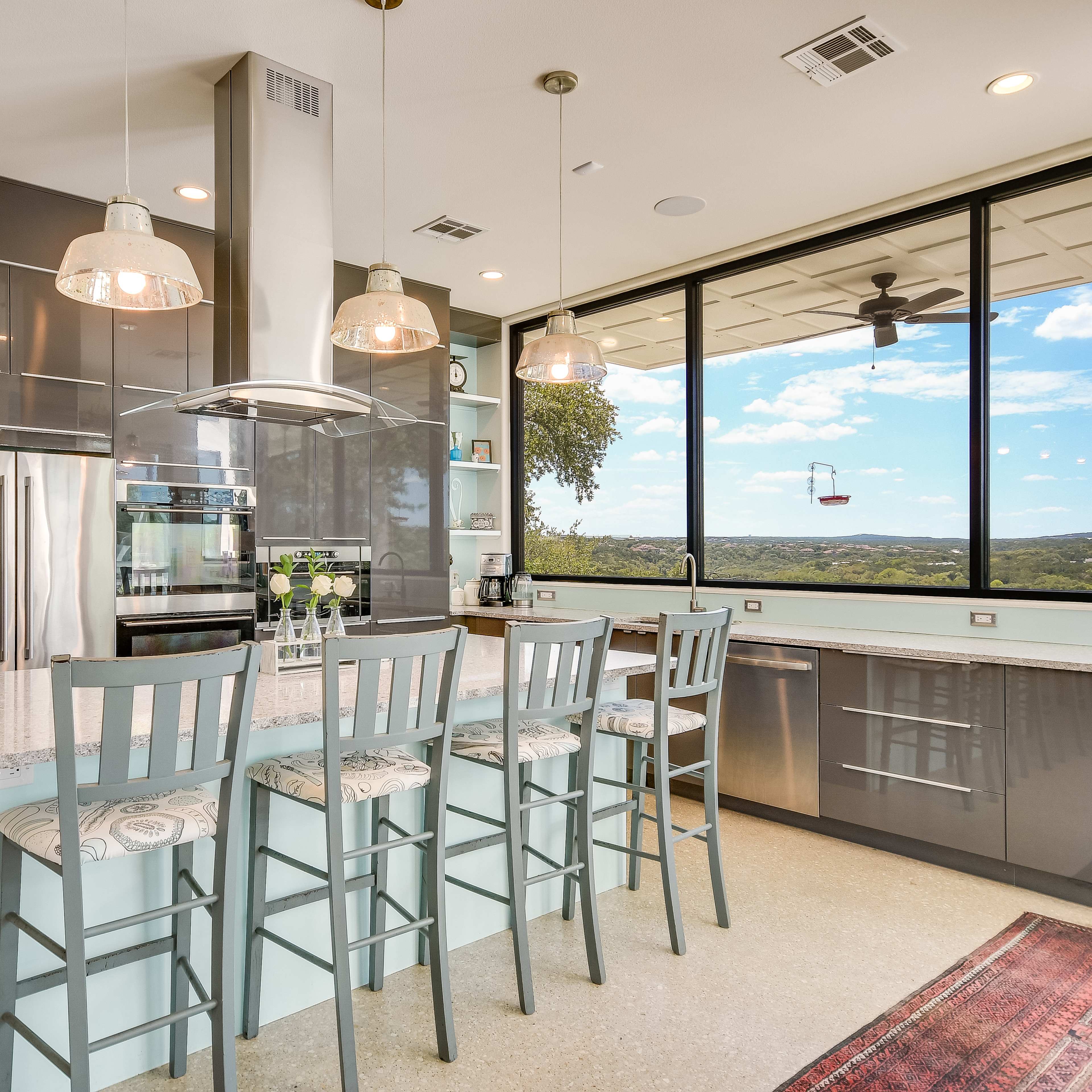 A modern kitchen features a large island with seating, stainless steel appliances, and a panoramic window overlooking a scenic view.
