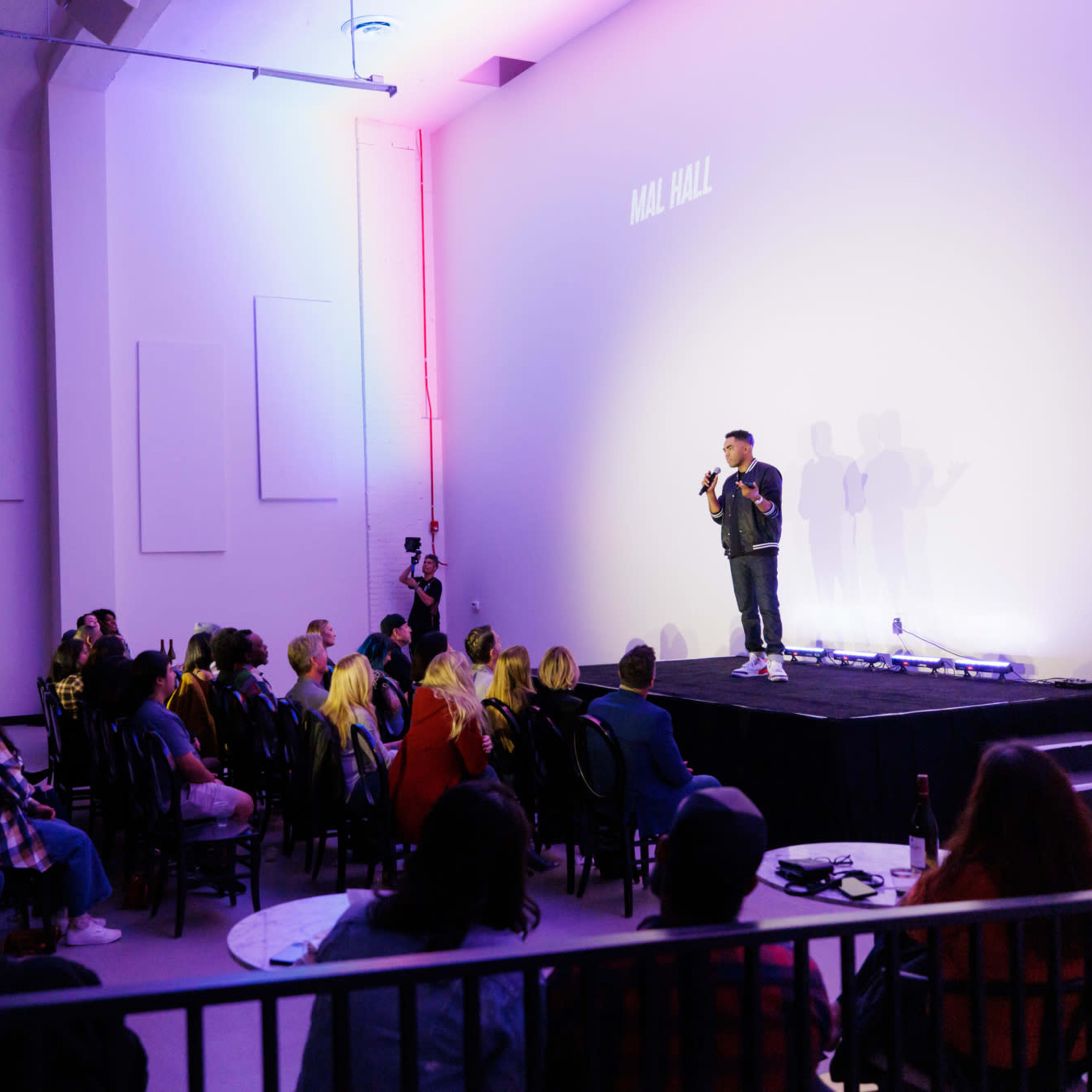 A speaker stands on stage in a dimly lit venue, addressing an audience seated at tables.