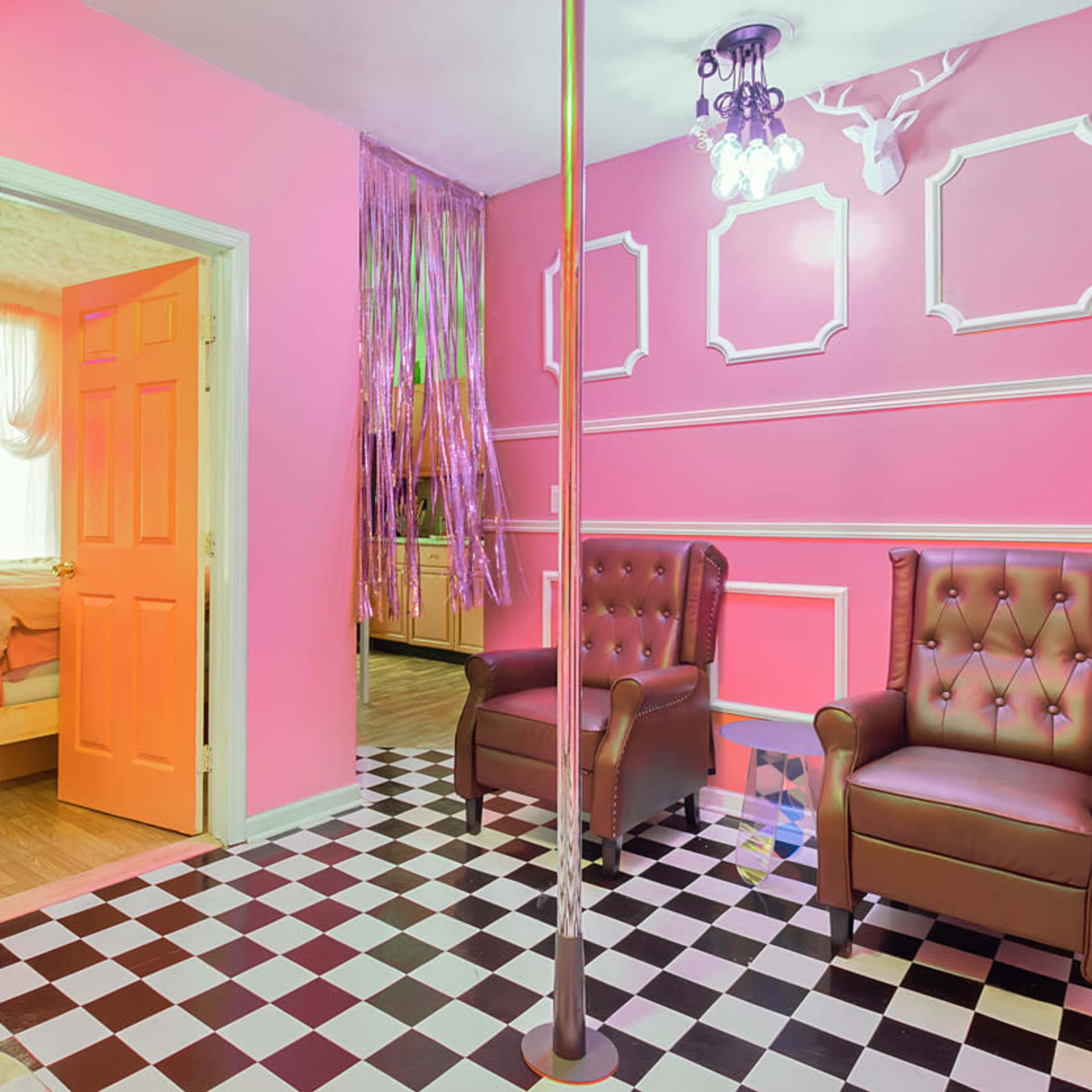 The room features pink walls, a checkered floor, two brown leather chairs, and a decorative mannequin holding a cake.