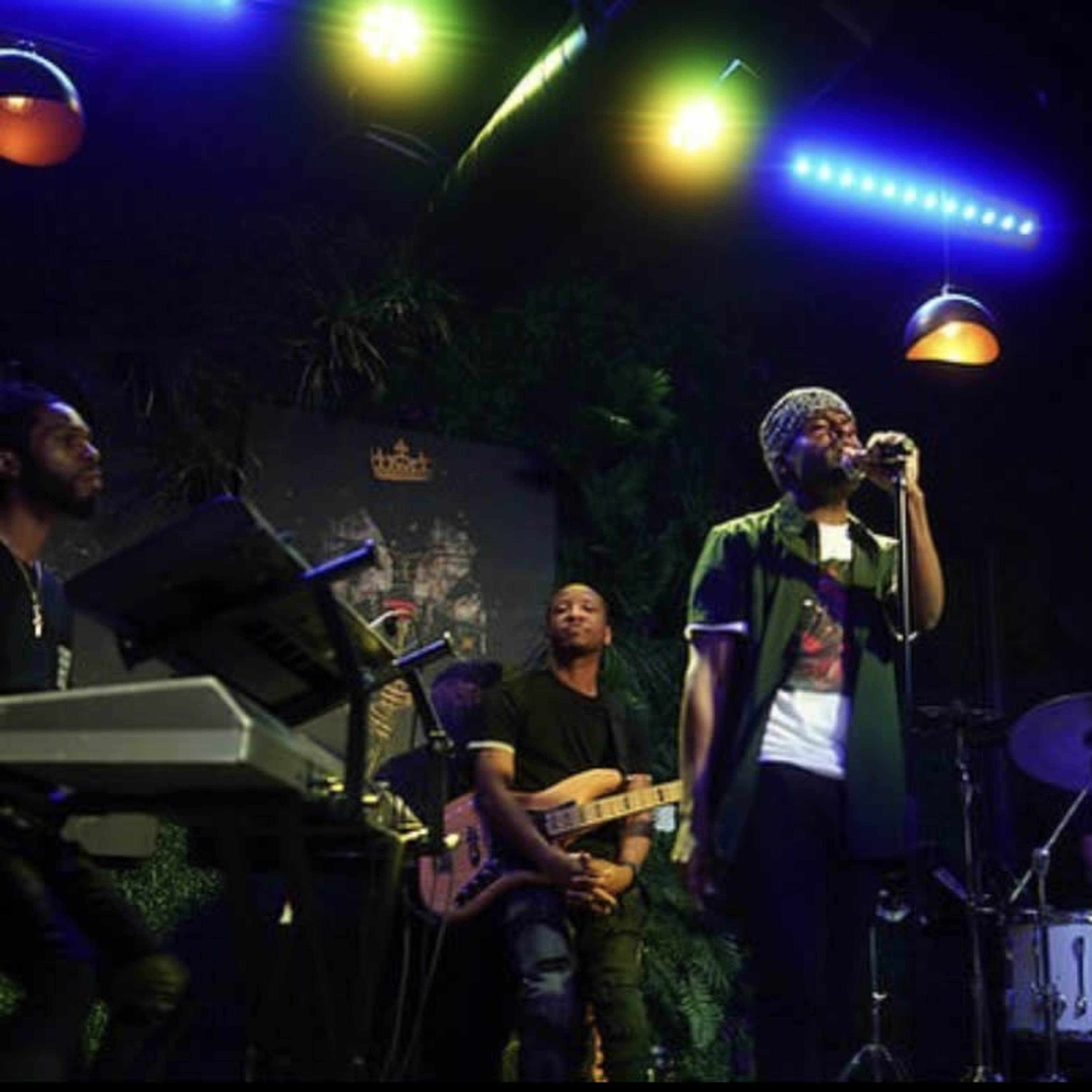 A small band performs on stage at a lounge with musicians playing instruments and a singer holding a microphone.