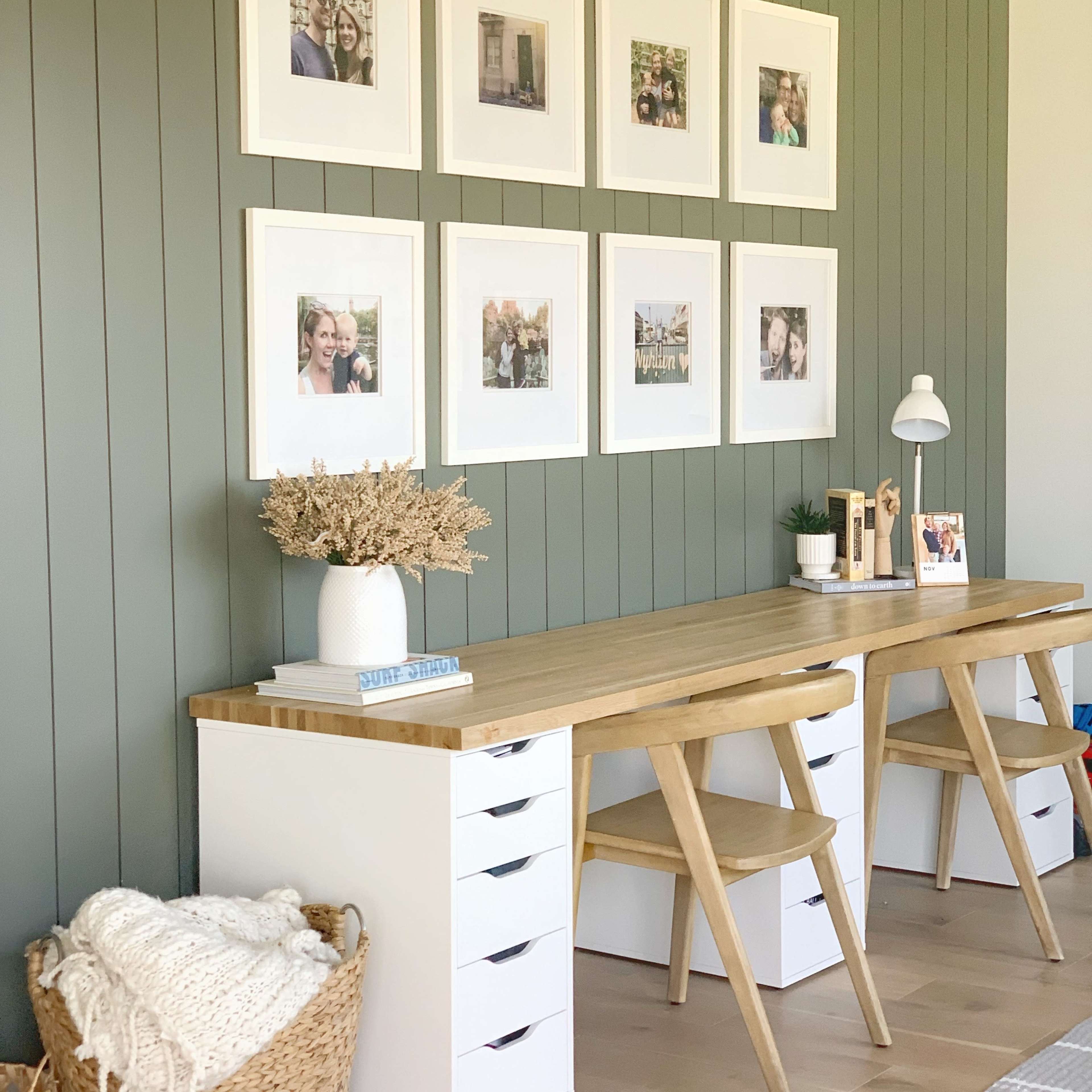 A neatly arranged home office with a wooden desk, two chairs, and a gallery wall of framed photographs above.