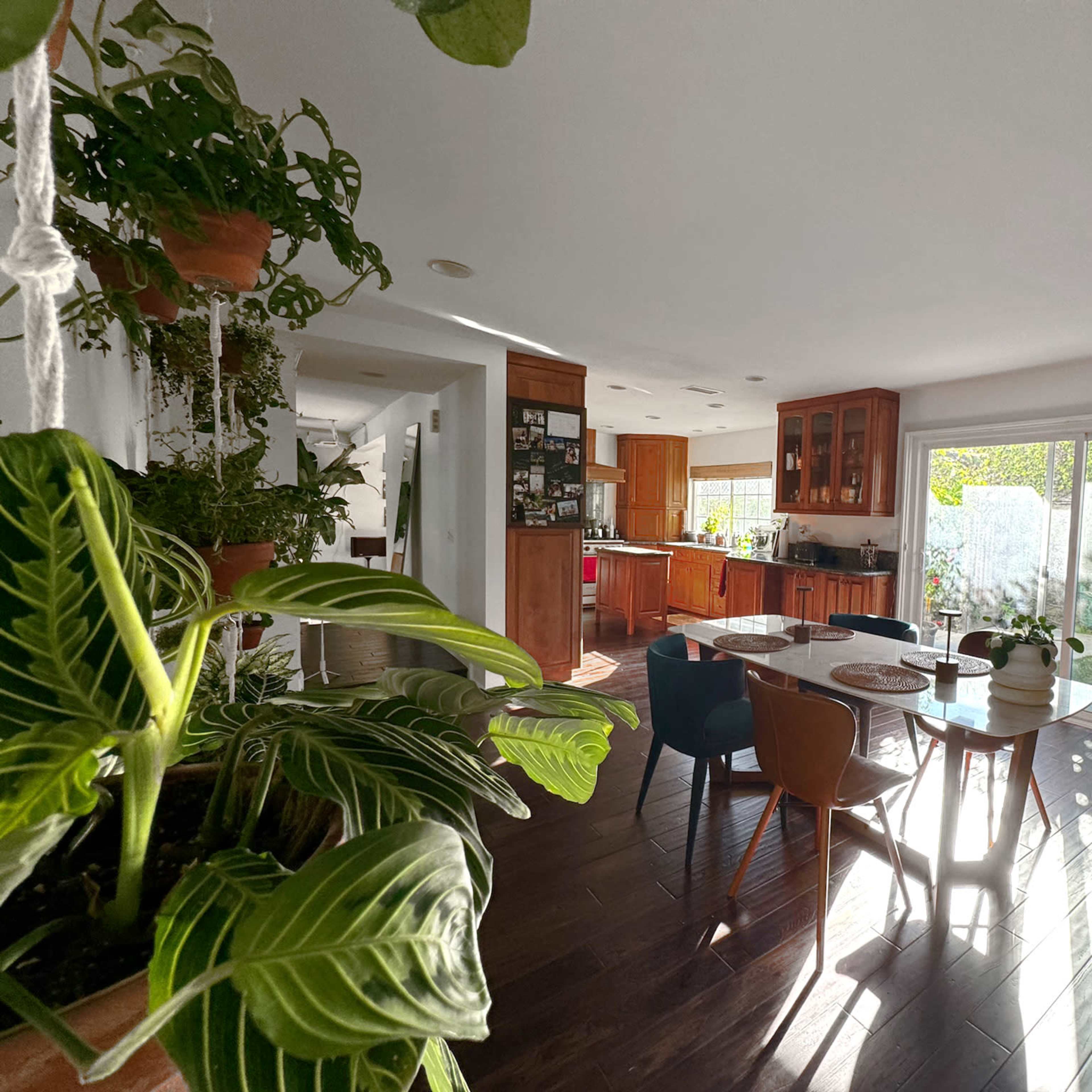 A well-lit dining area features a table set for meals, surrounded by chairs, with a view of a garden through sliding glass doors.