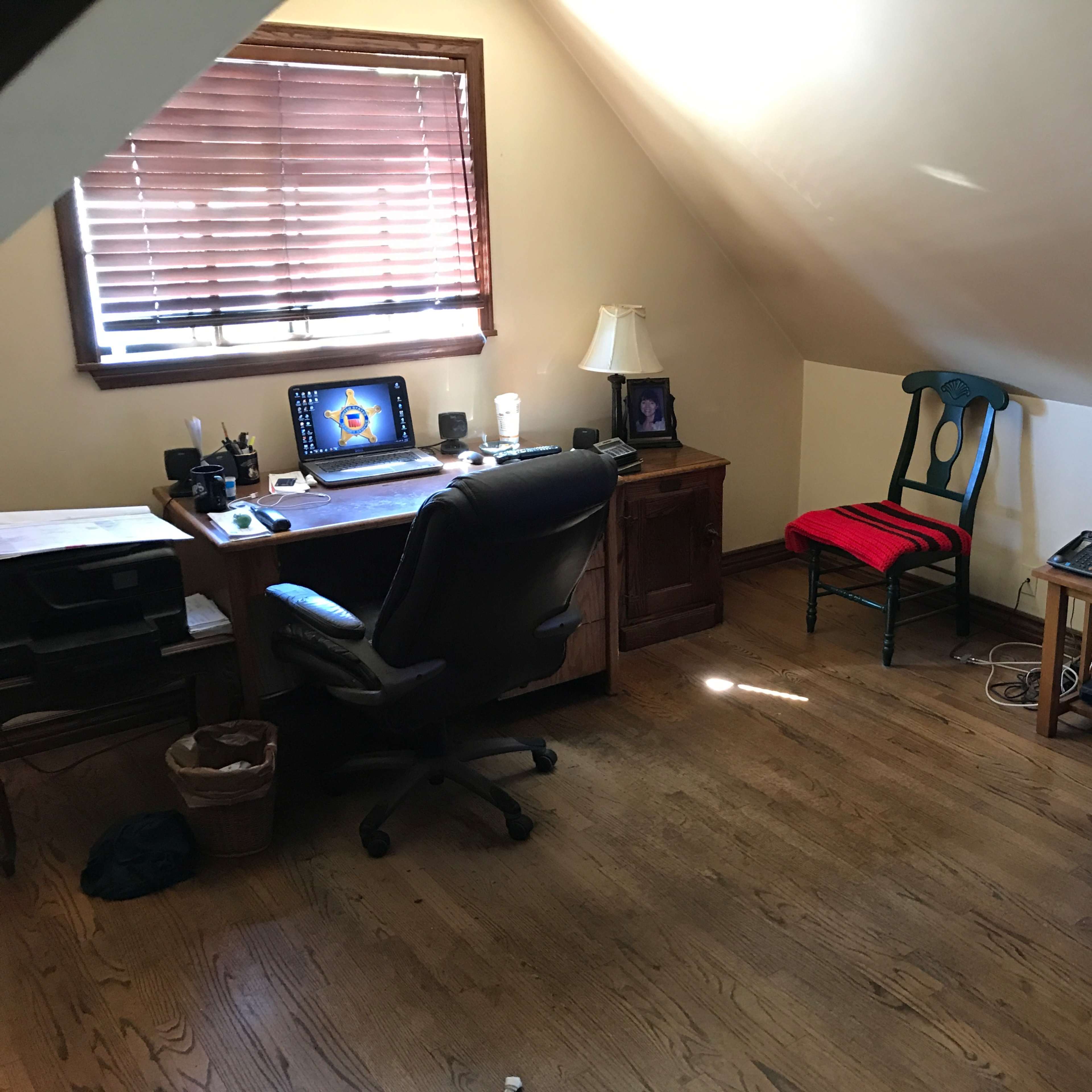 A small attic office with a wooden desk, a black office chair, a television, and a red chair against a slanted ceiling.