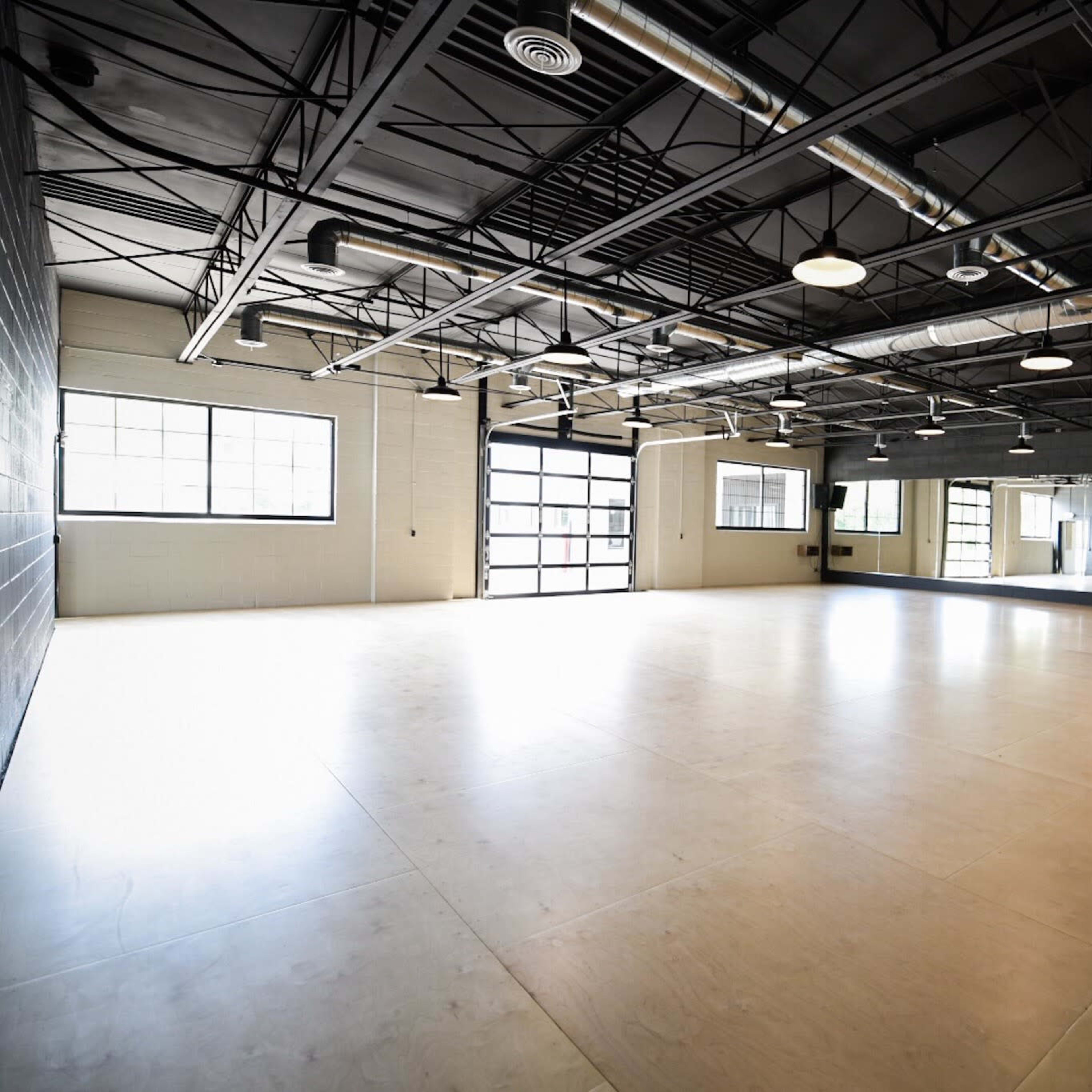 A spacious, empty dance studio with wooden flooring and large windows.