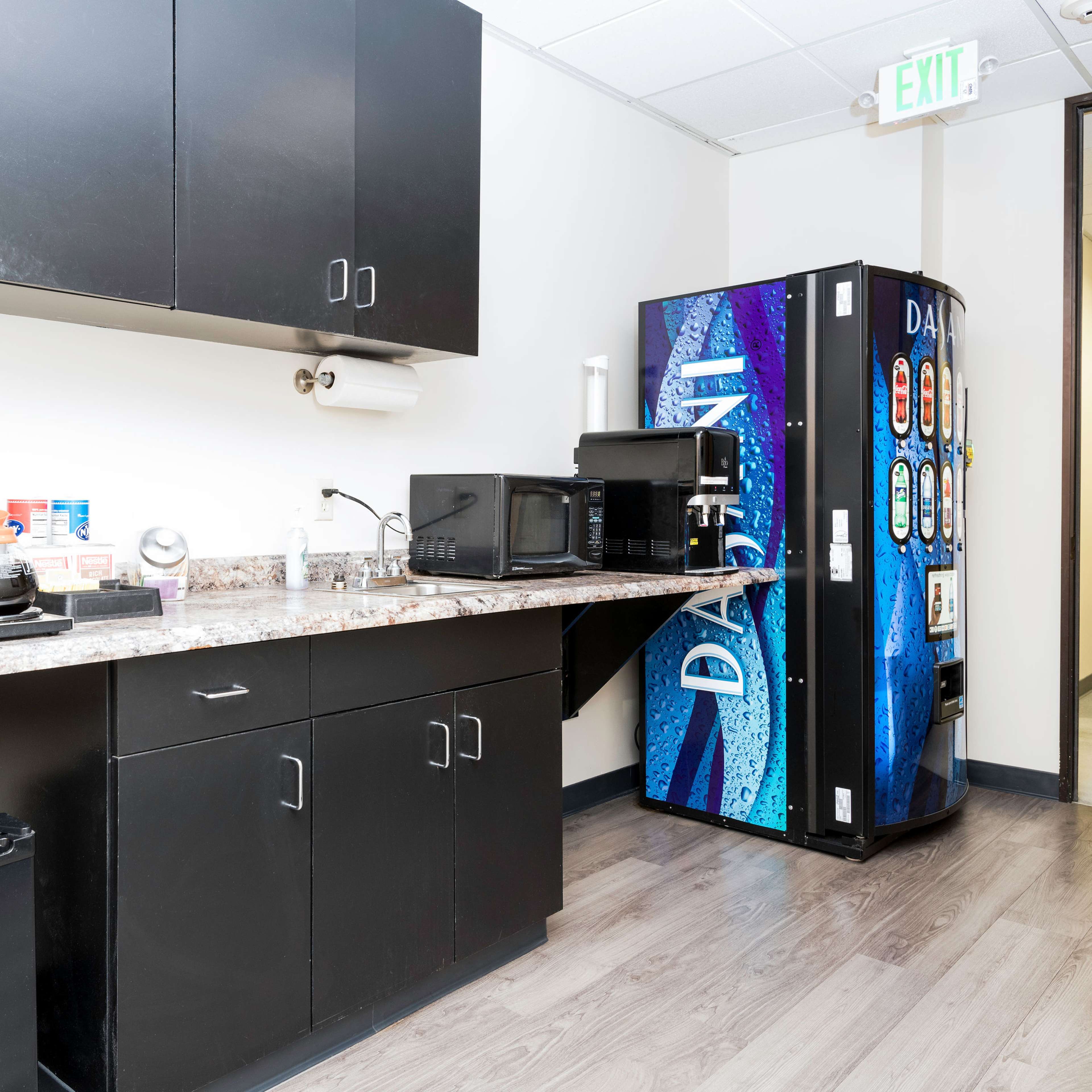 A kitchenette with a coffee maker, two microwaves, a small refrigerator, and a vending machine along a countertop.