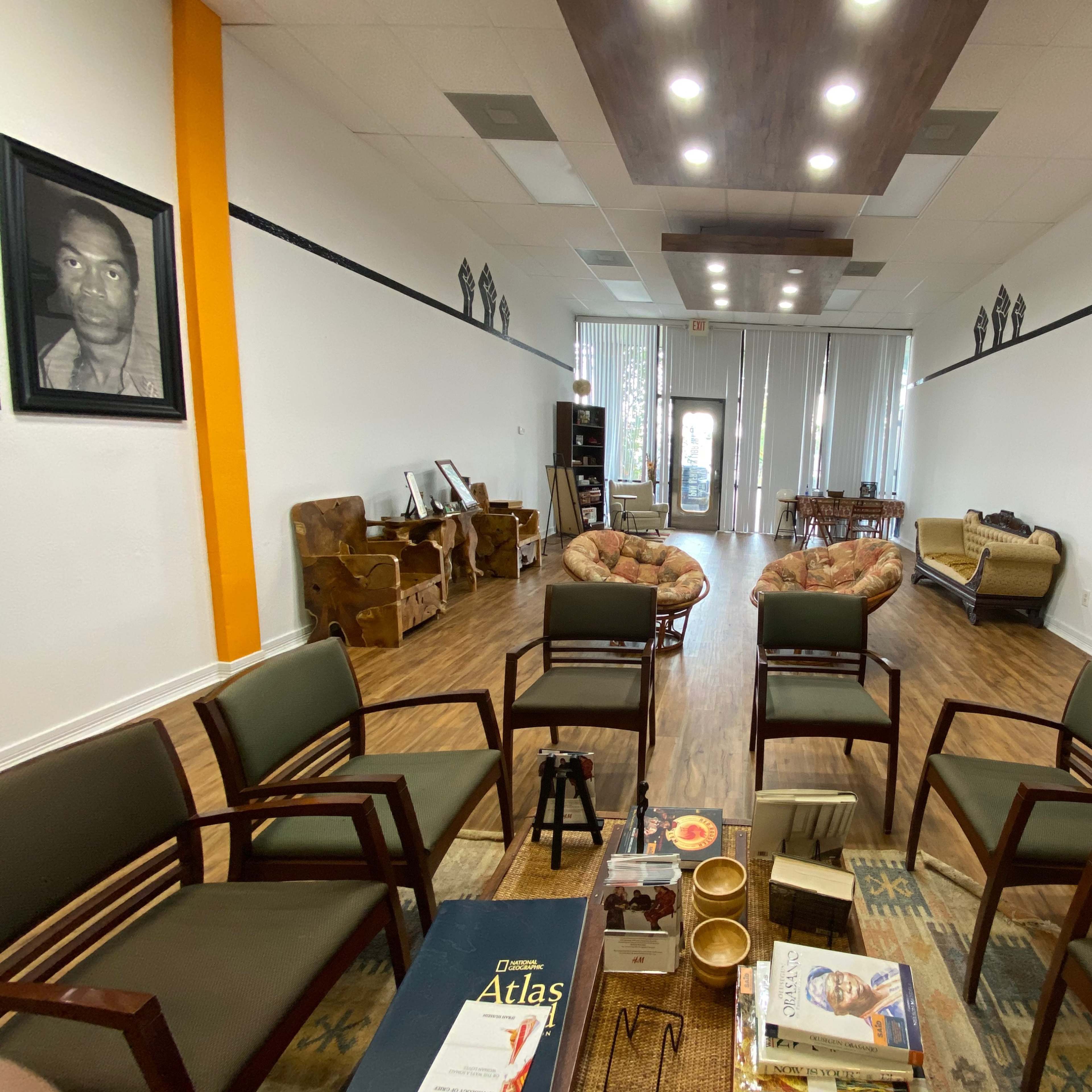 A spacious waiting area with several chairs arranged around a coffee table, framed portraits on the walls, and various seating options along the sides.