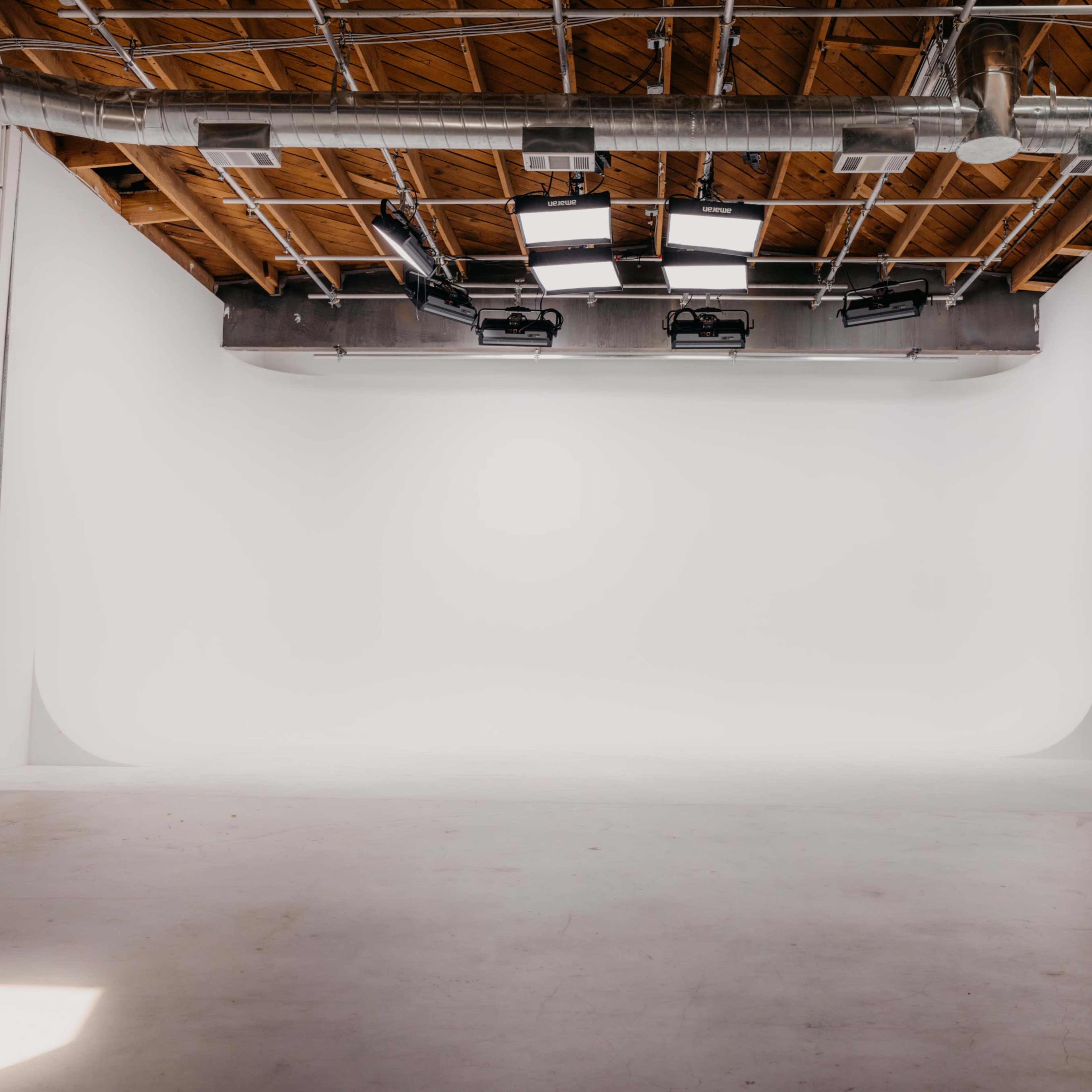An empty studio space with a seamless white backdrop and overhead lighting.