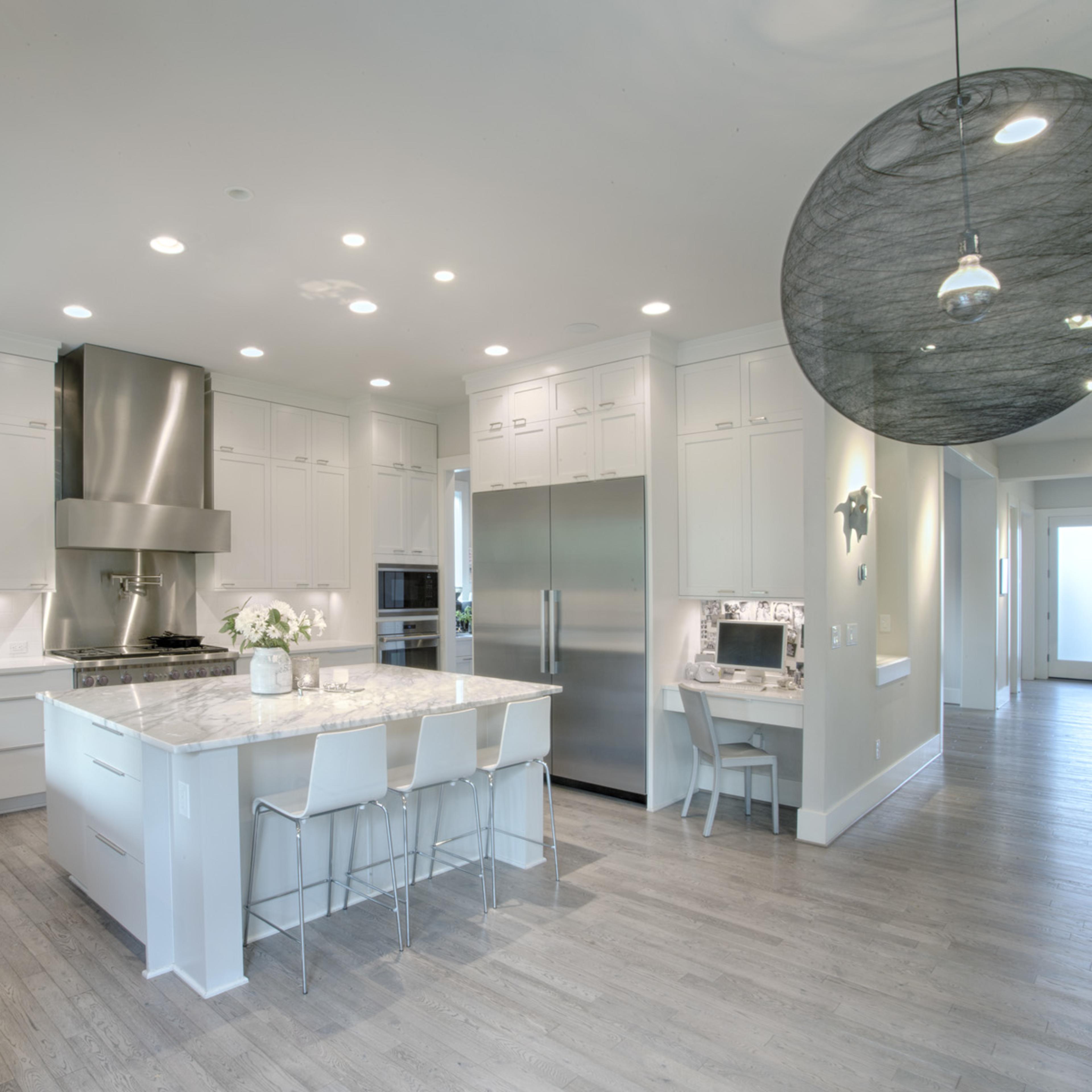 A modern kitchen features white cabinetry, a large island with seating, stainless steel appliances, and a light wood floor.