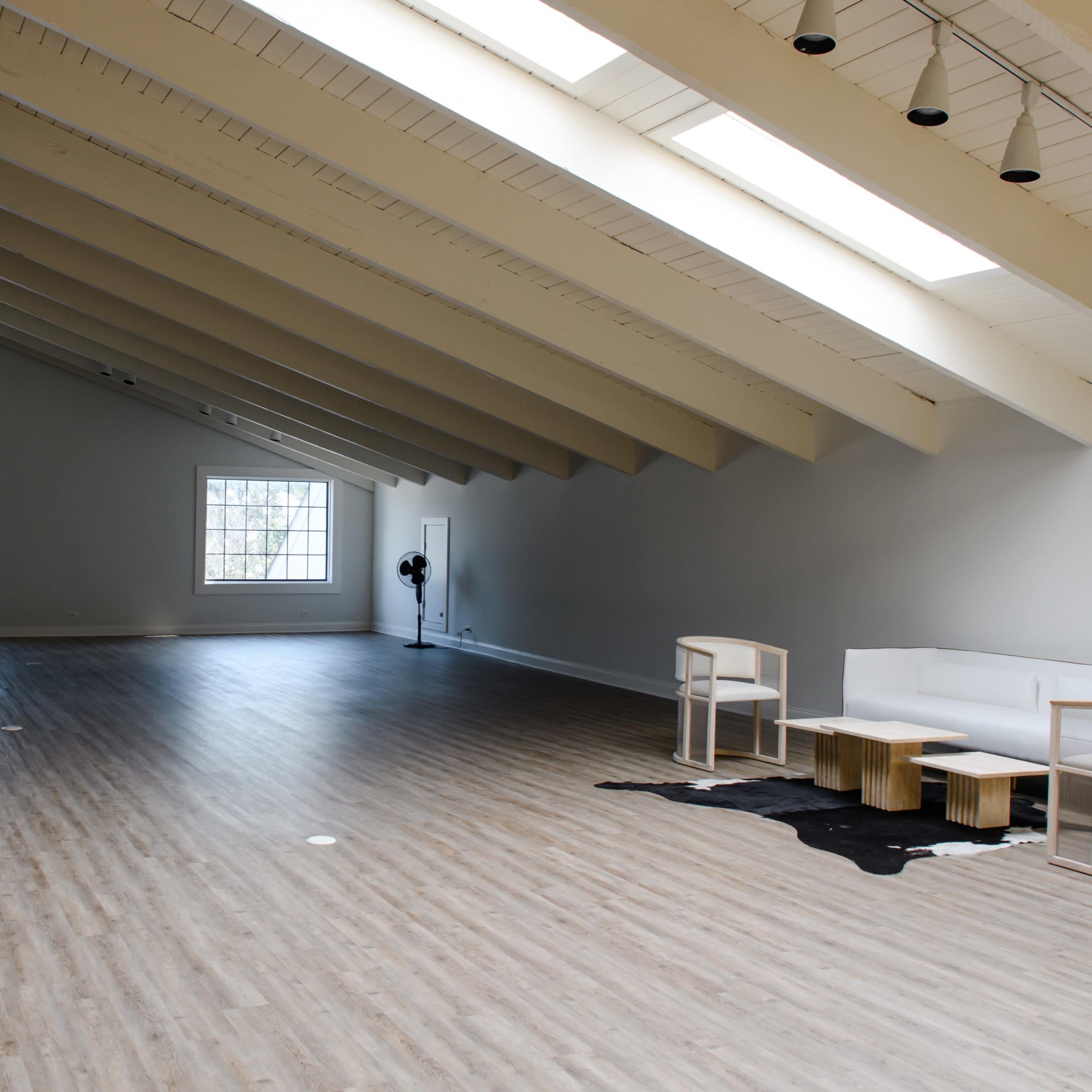 A spacious, well-lit room with high sloped ceilings, featuring wooden flooring, a white sofa, and minimalist furniture.