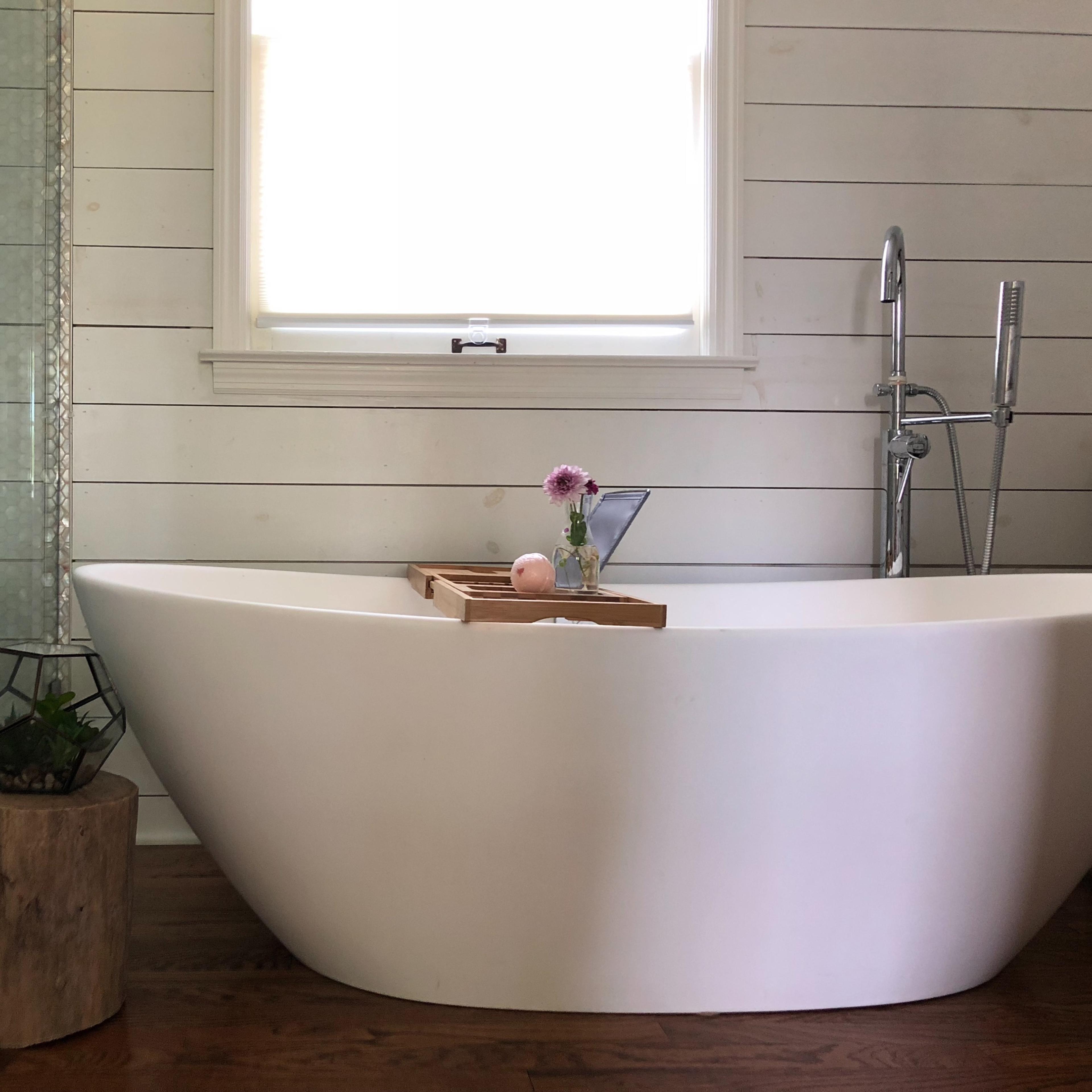 A freestanding white bathtub is positioned next to a glass shower in a bathroom with wooden accents and a window above it.