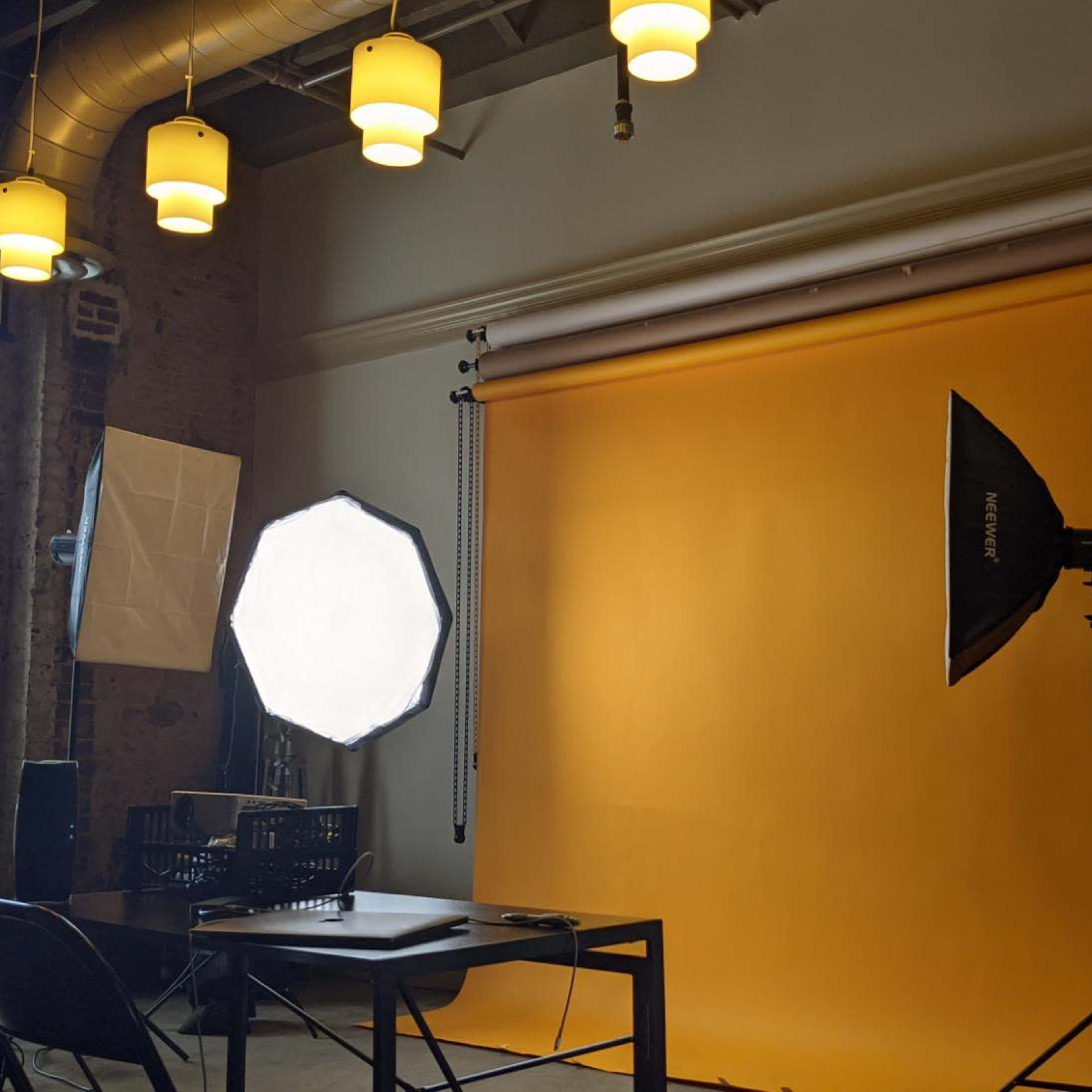 A photography studio setup with a yellow backdrop, softbox lights, and a table in front of the backdrop.
