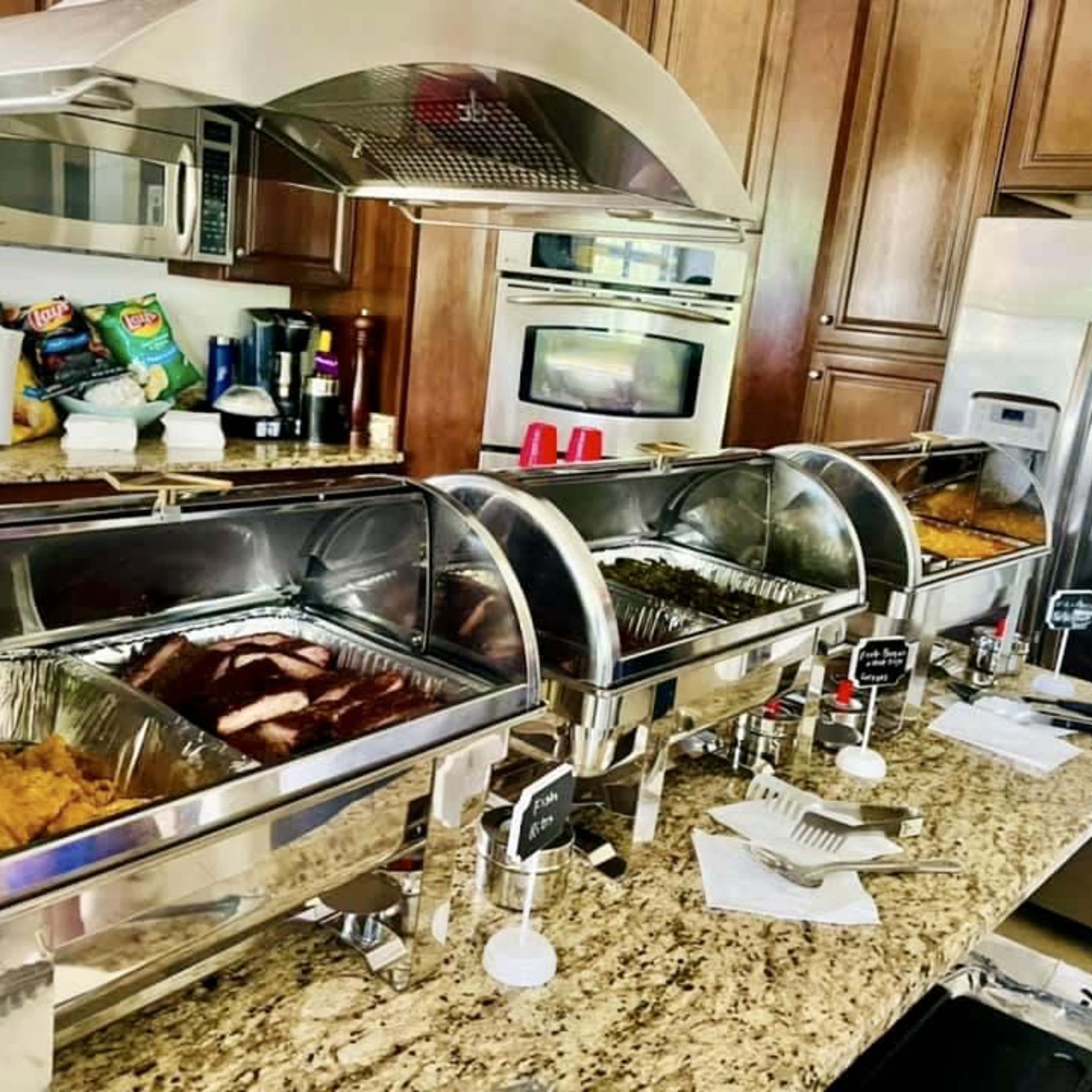 A kitchen counter with three chafing dishes containing various dishes, along with utensils and condiments.