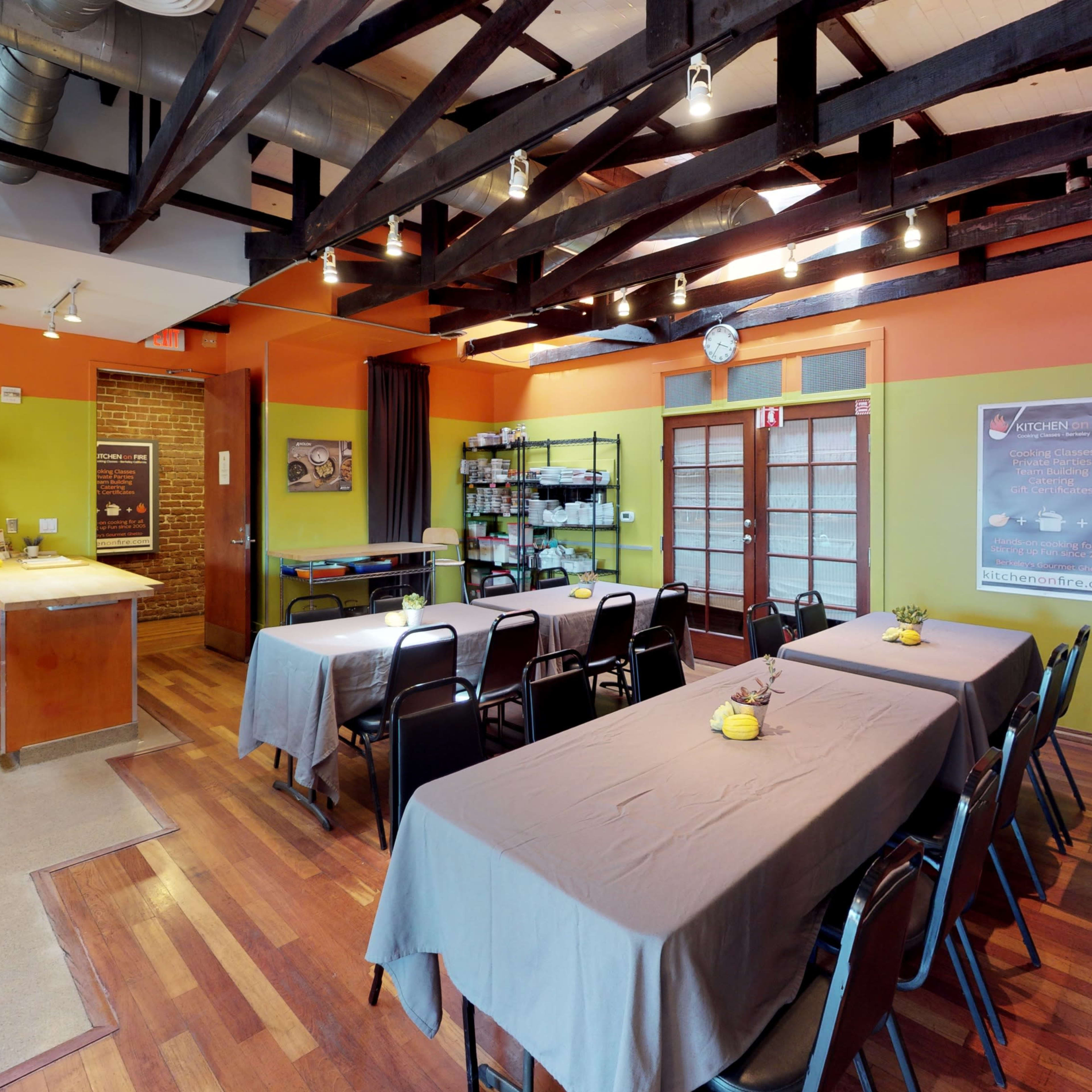 A spacious meeting room with long tables covered in gray cloths, surrounded by black chairs, under a ceiling with exposed wooden beams.