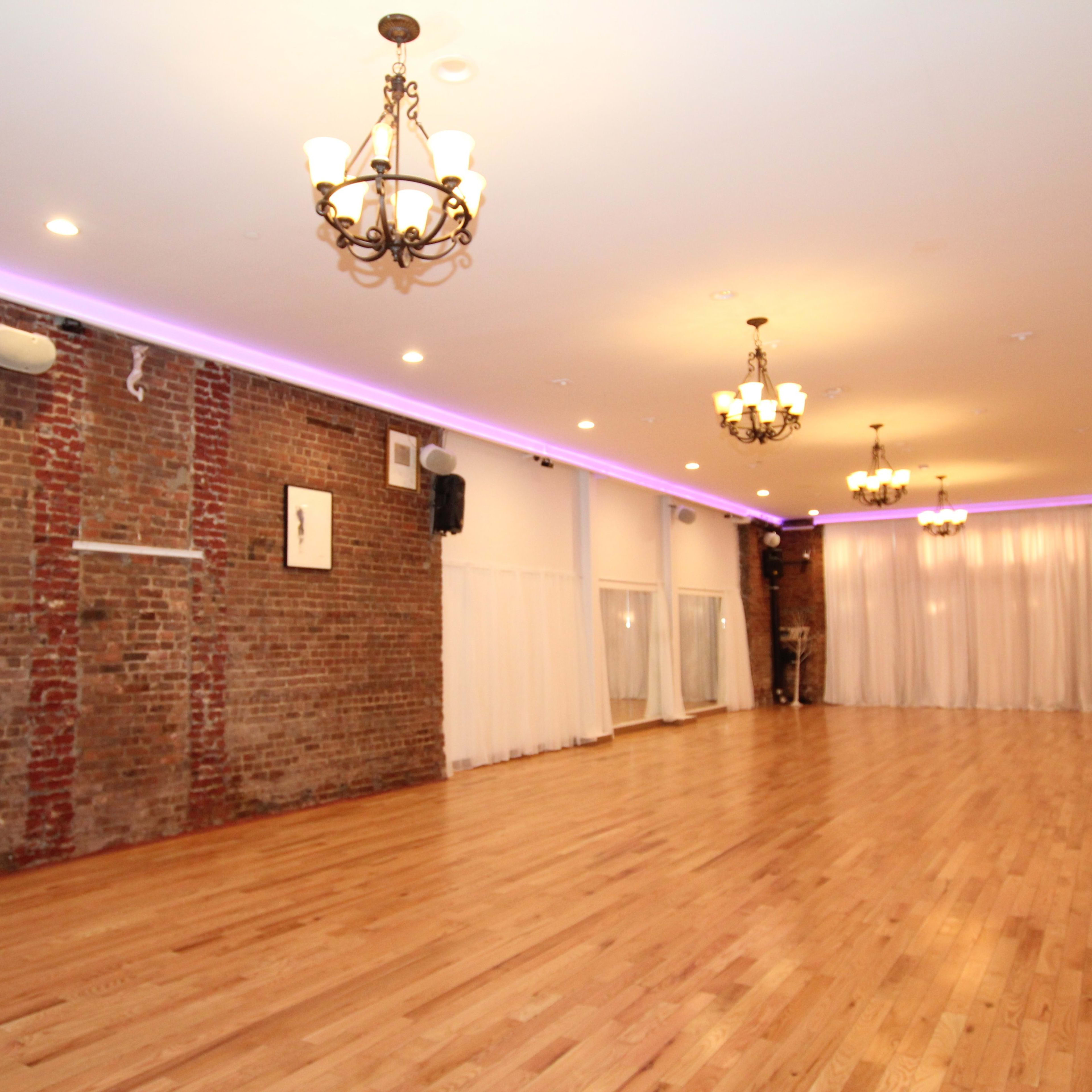 A spacious indoor venue with exposed brick walls, hardwood flooring, and chandeliers, illuminated by soft lighting.