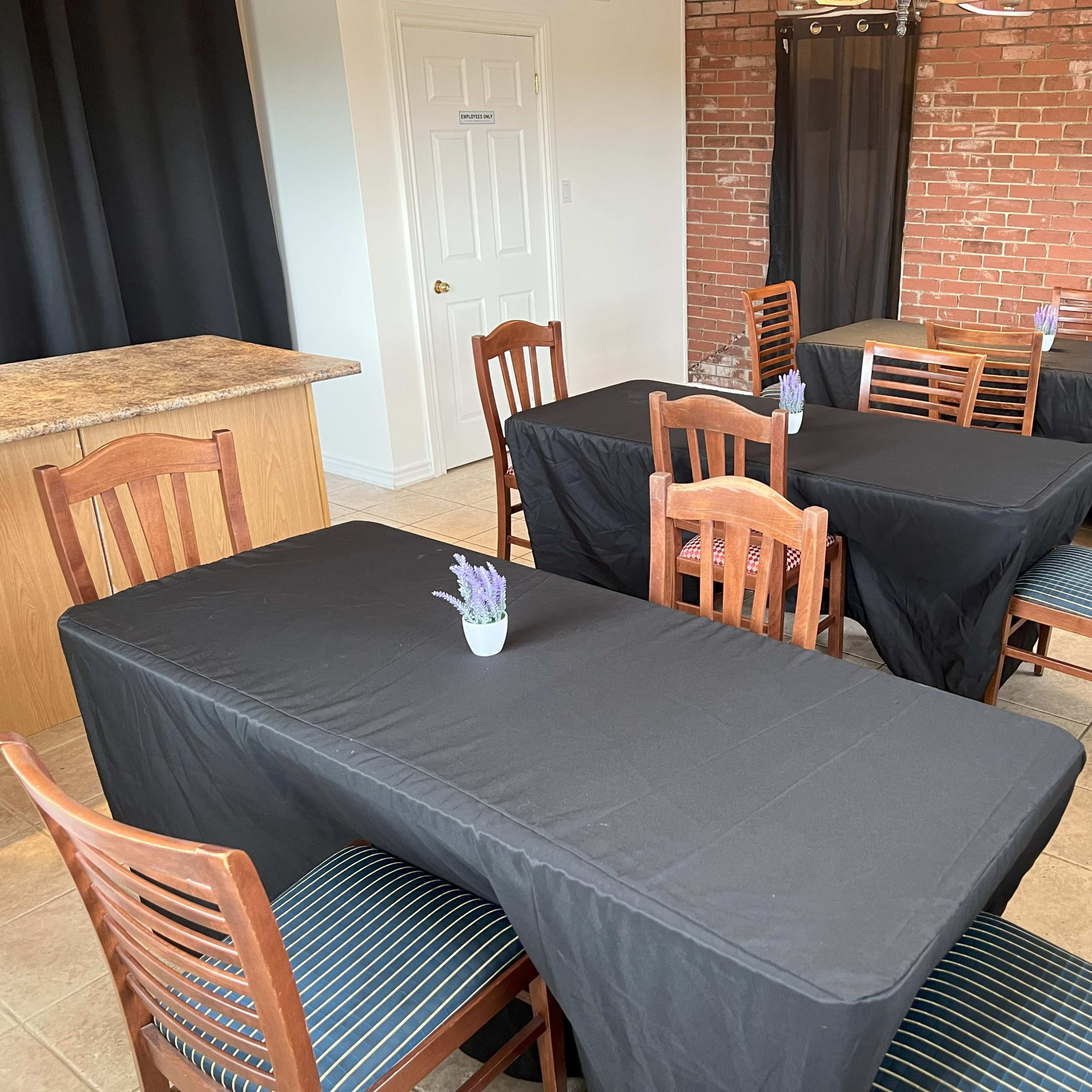 A room with several tables covered in black tablecloths and wooden chairs, arranged around a small vase with lavender on each table.