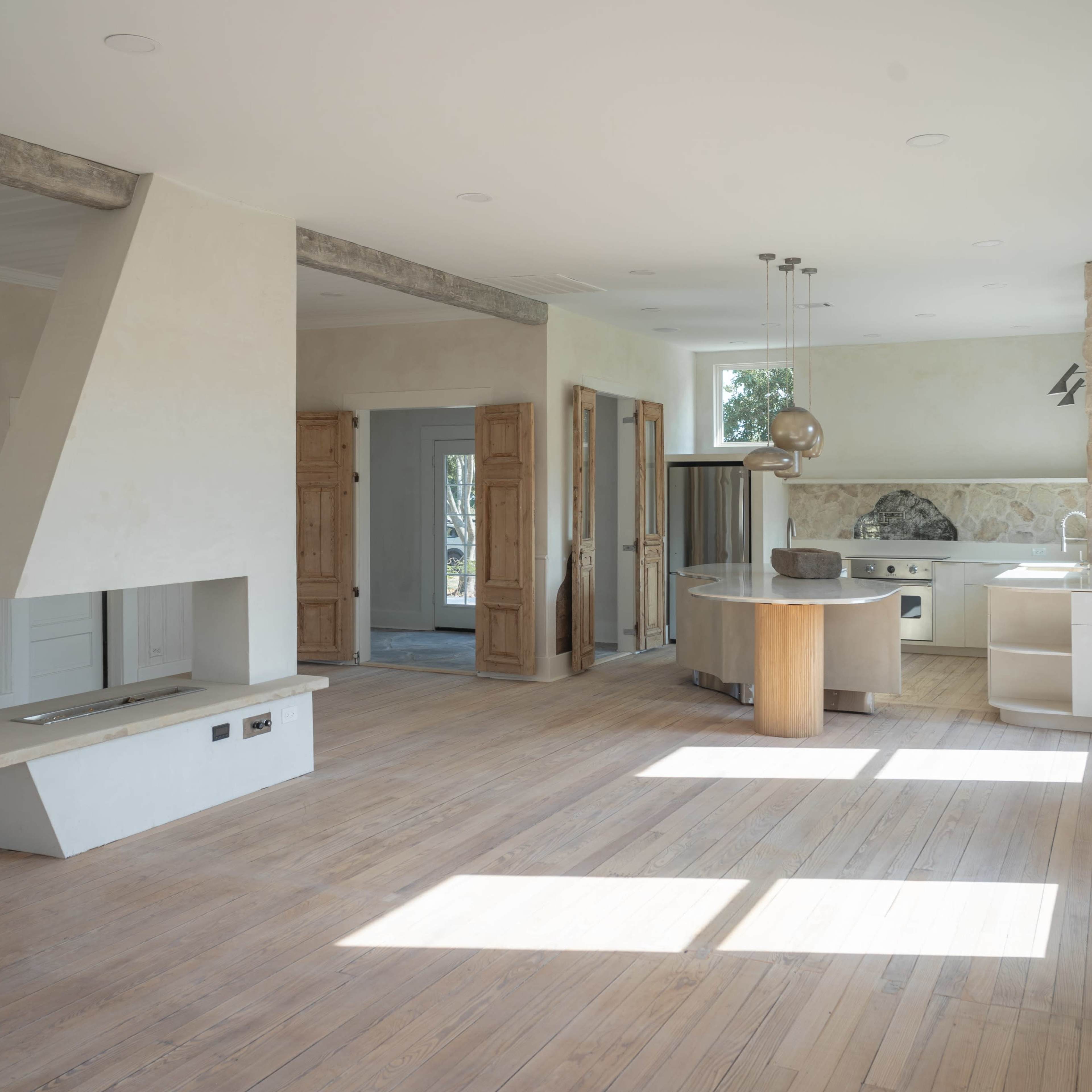 A spacious, unfinished interior of a modern house with wooden floors, large windows, and a kitchen area integrated into the main living space.