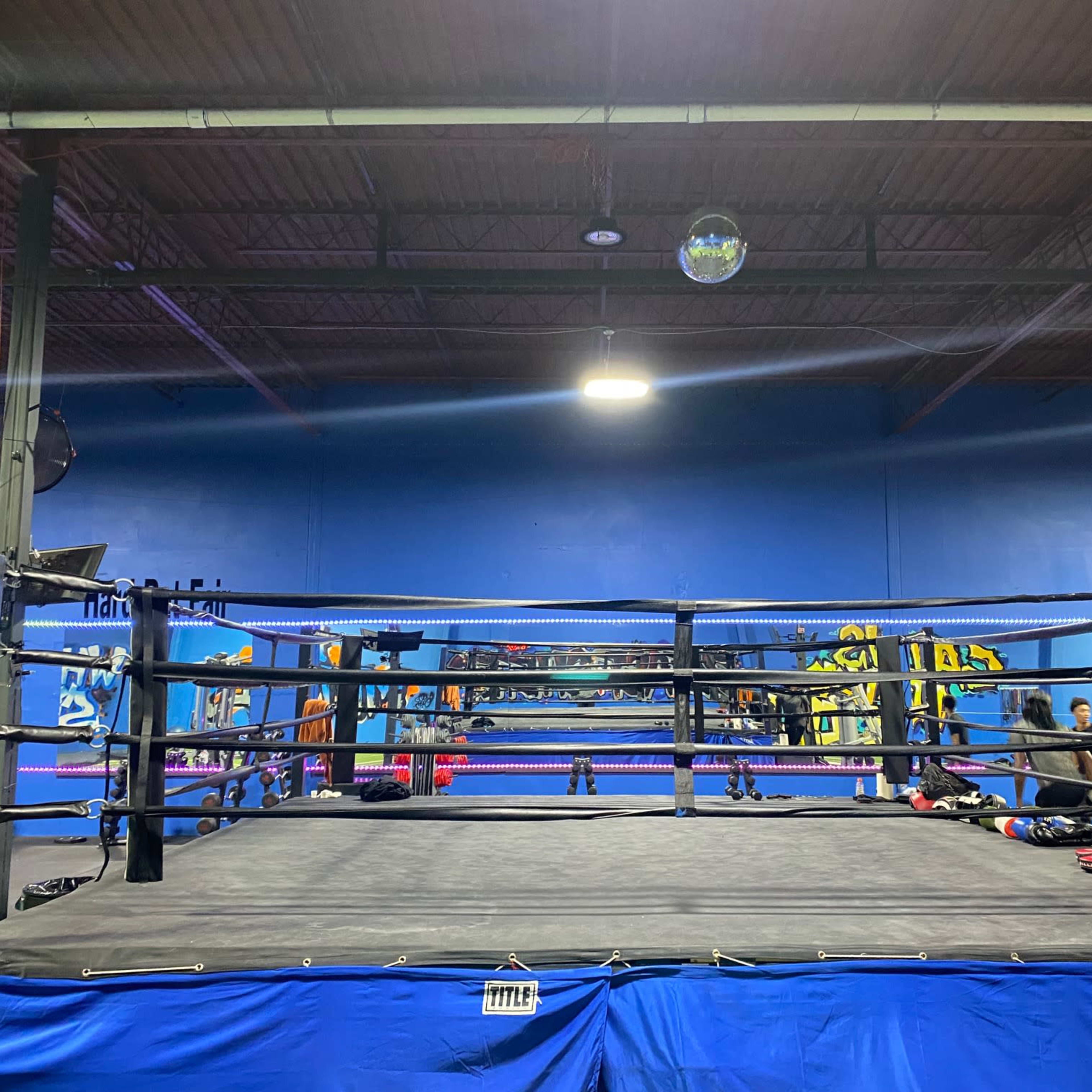 A boxing ring surrounded by various gym equipment in a training facility.