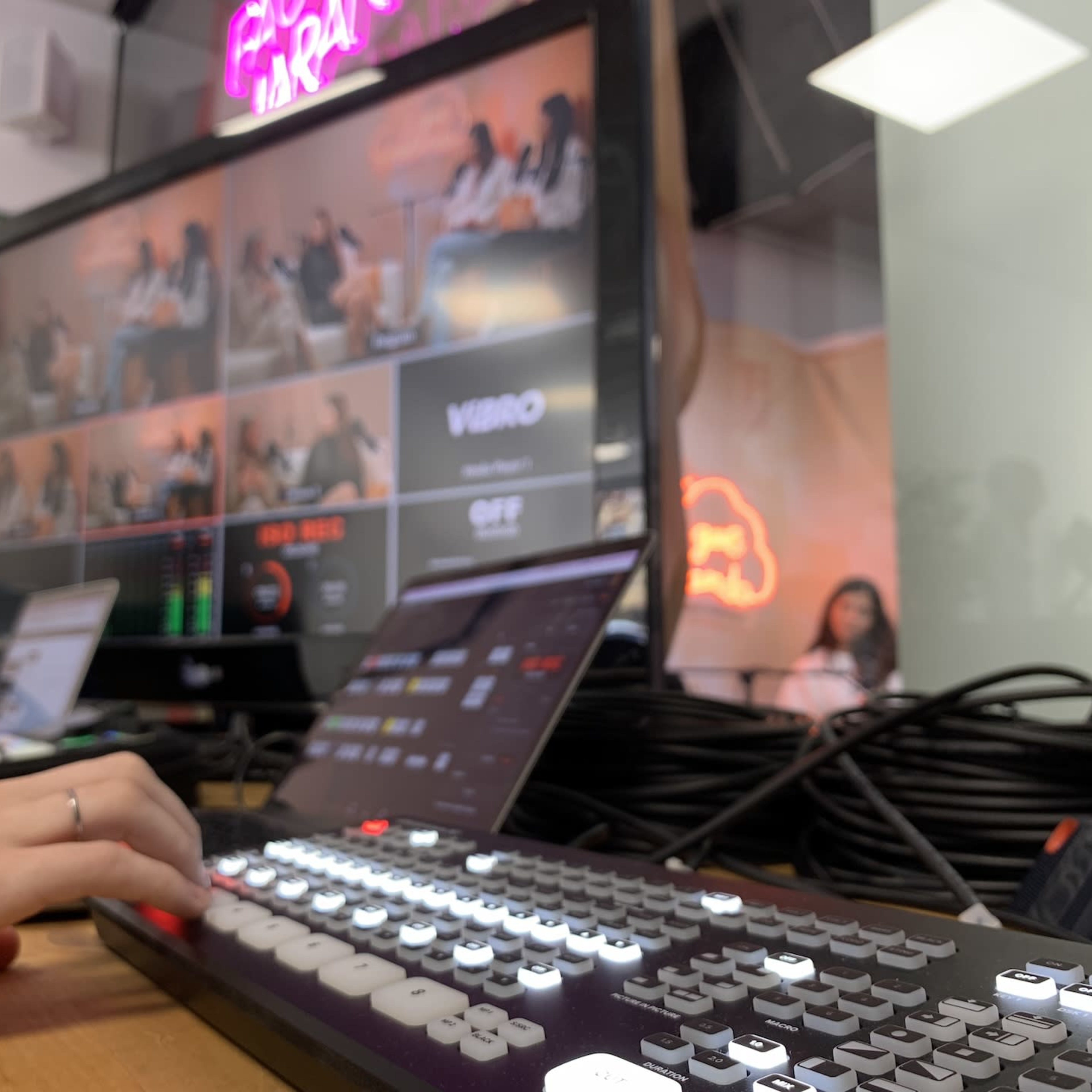 A person is operating a video switcher in front of a large screen displaying multiple camera feeds in a production studio.
