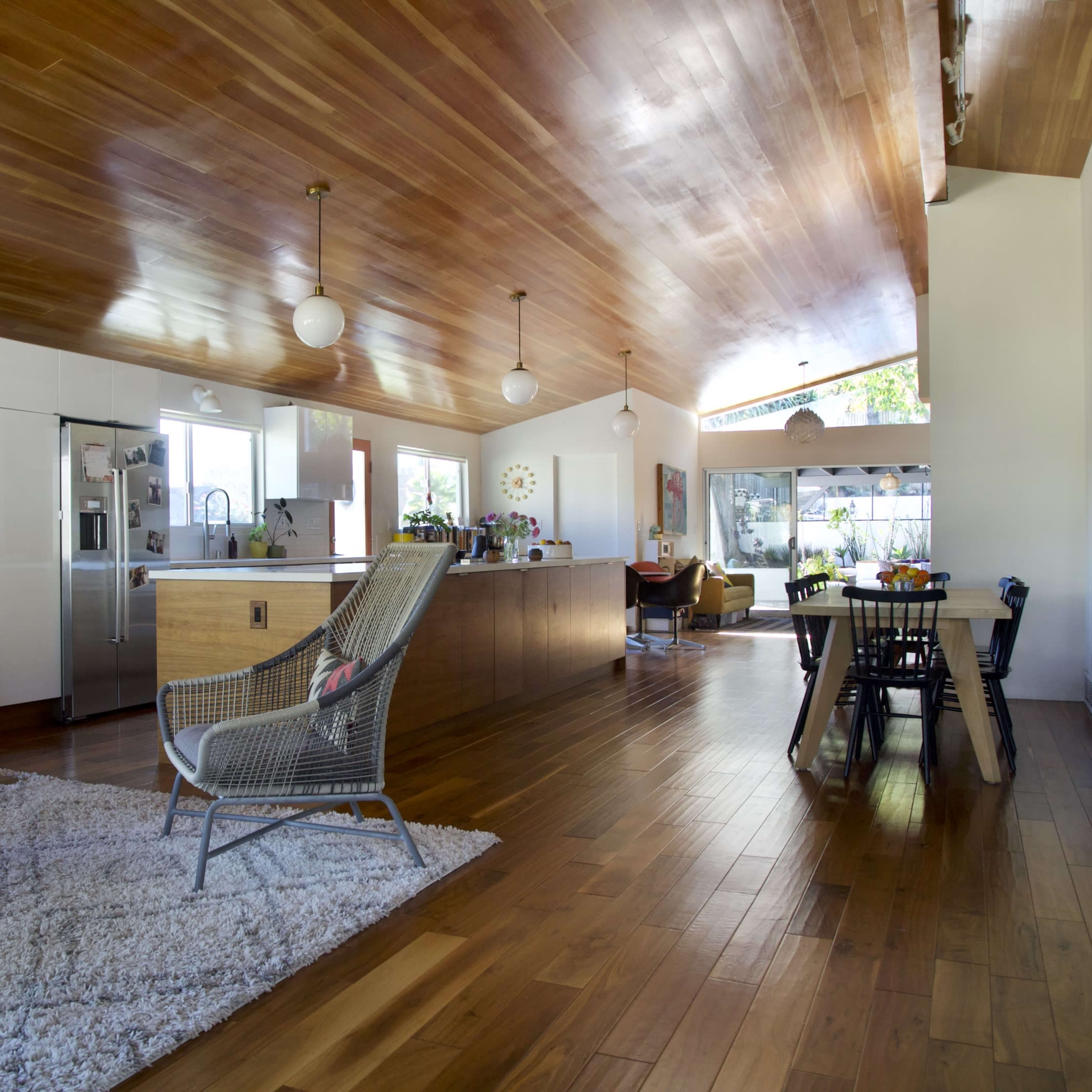 A spacious, modern living area featuring a wooden ceiling, a kitchen with an island, and a dining area adjacent to large windows.