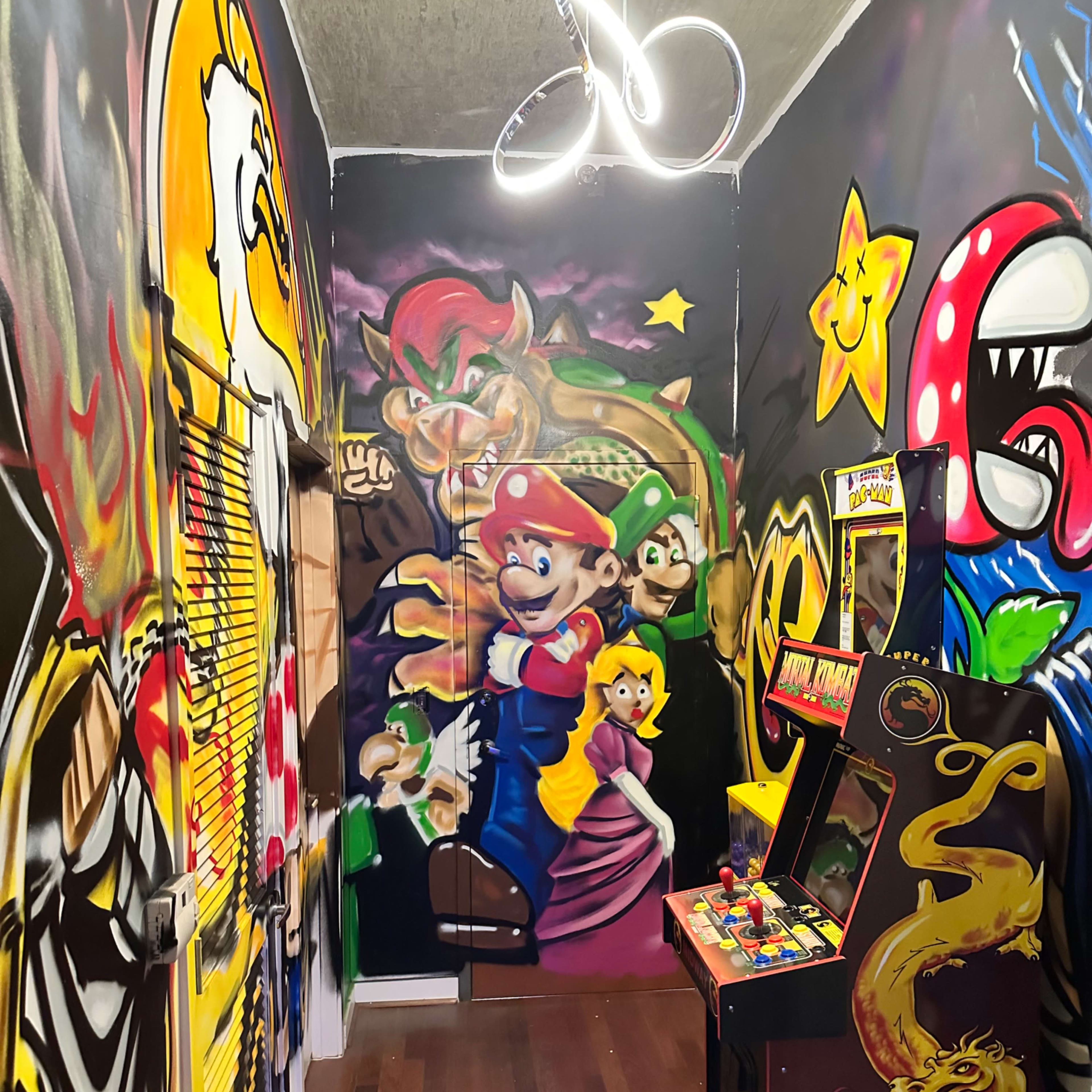 The room features colorful graffiti art on the walls depicting iconic video game characters, along with a classic arcade machine in the corner.