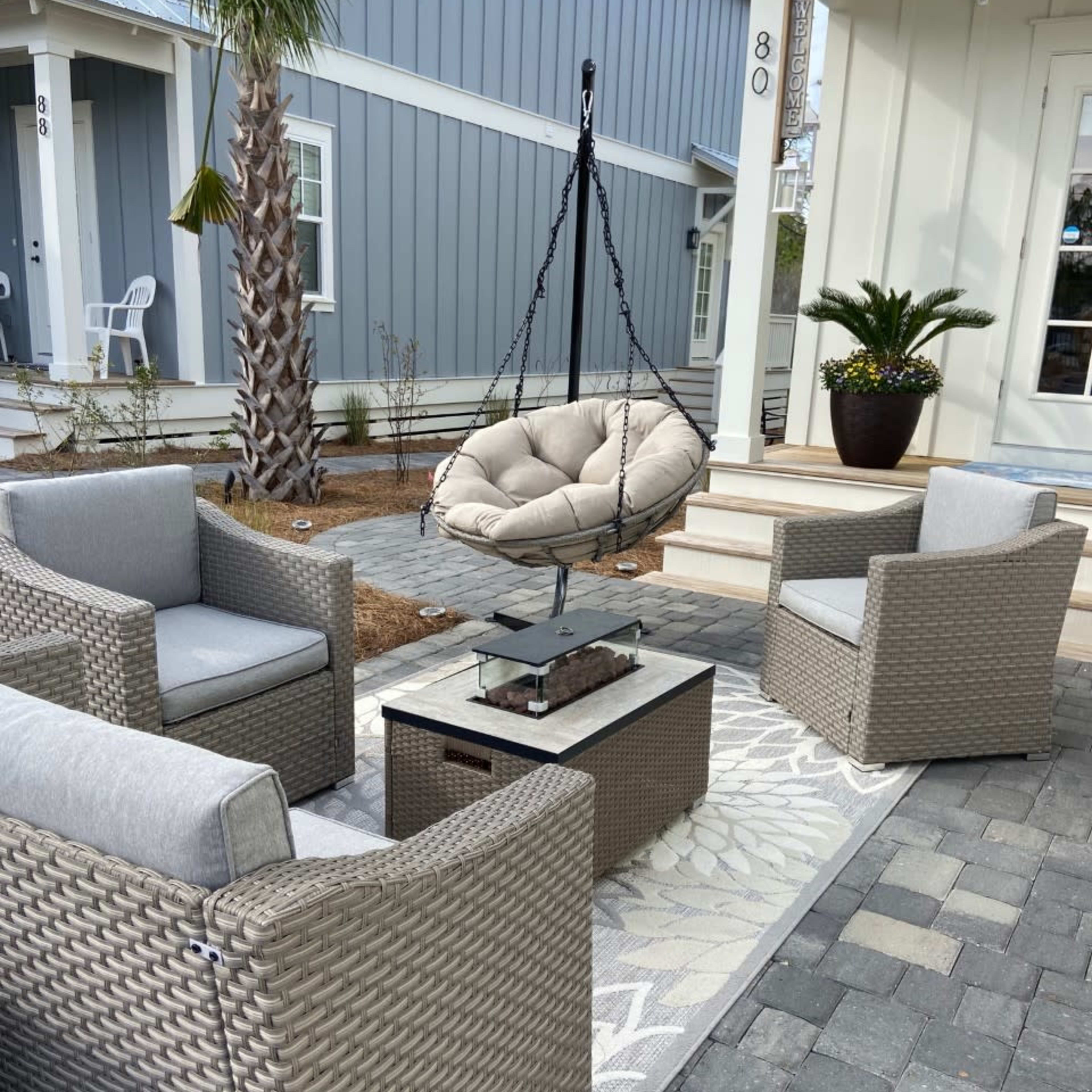 A cozy outdoor seating area with four wicker chairs surrounding a small table and a hanging chair suspended nearby.