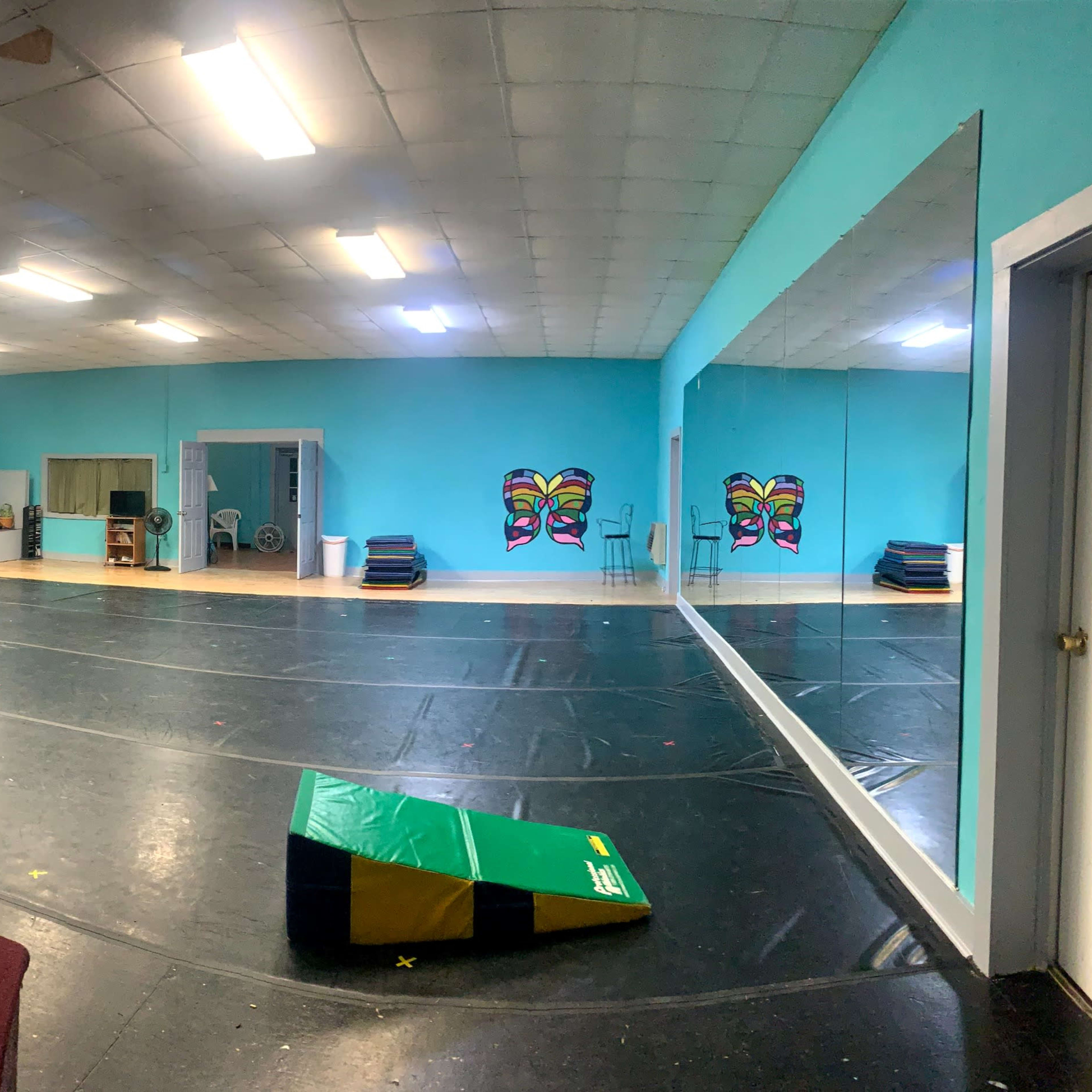 A spacious dance studio with turquoise walls, a black floor, and mirrored walls, featuring a red carpet area and various colorful decorations.