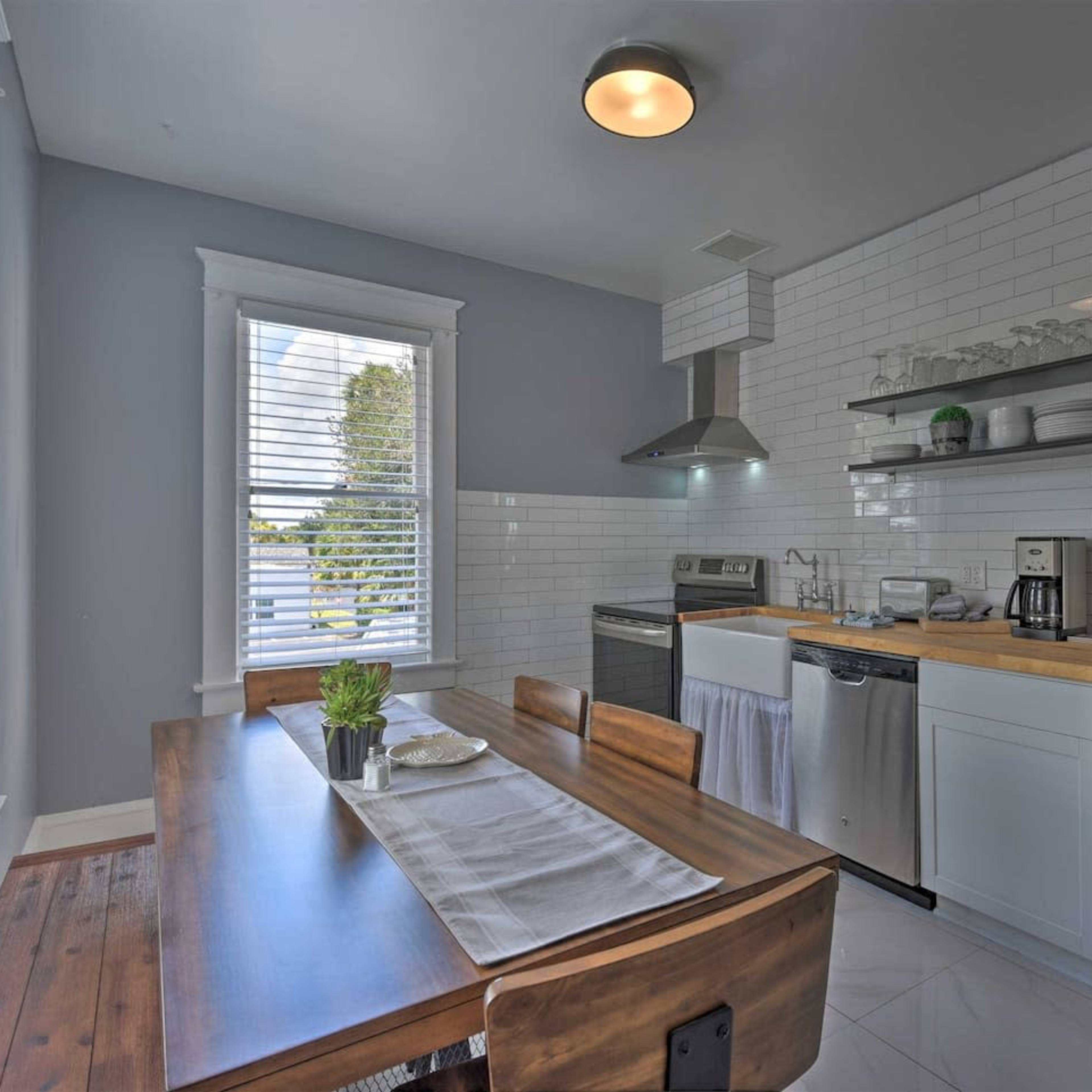 A modern kitchen with white tile walls, a wooden dining table, stainless steel appliances, and a minimalistic design.
