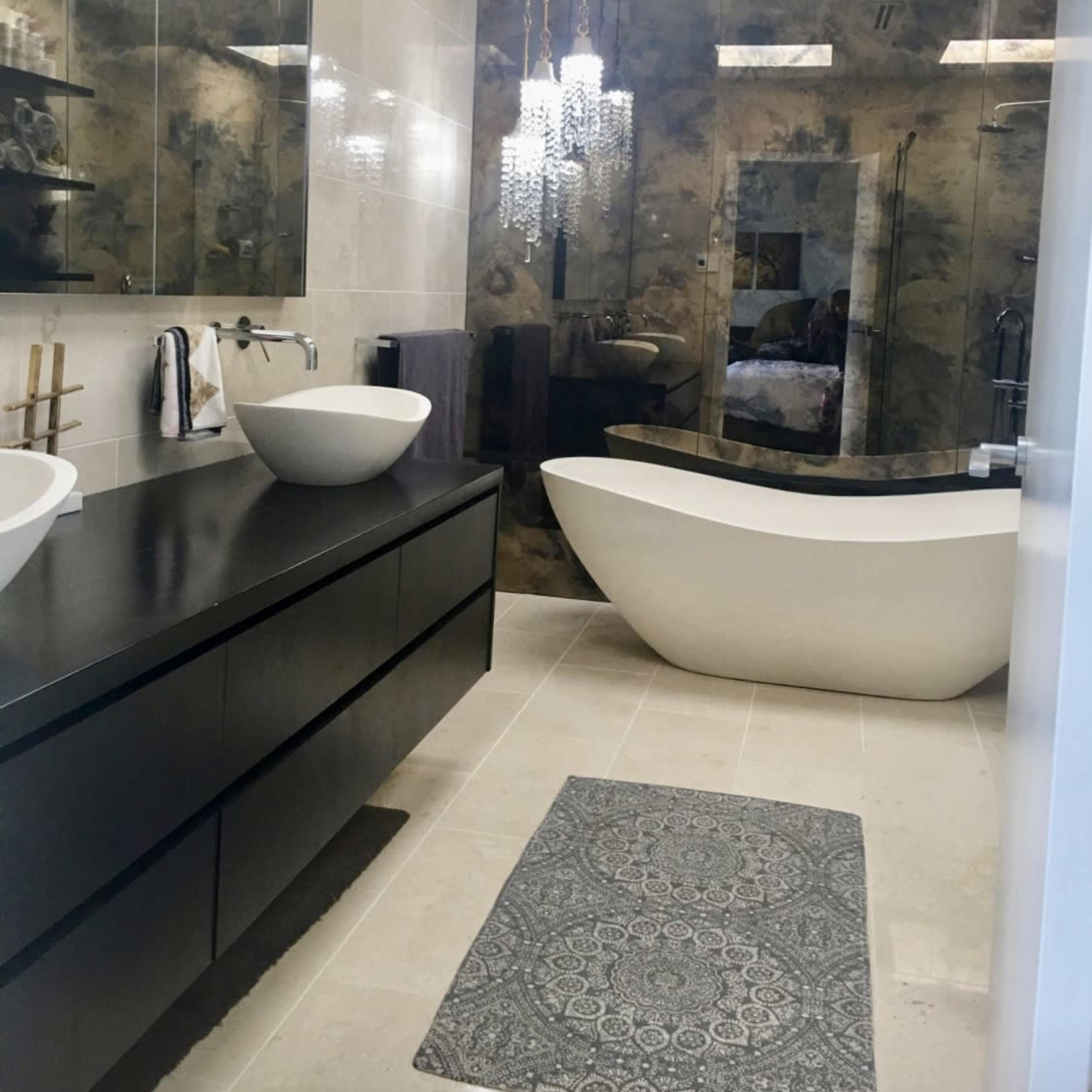 A modern bathroom featuring a freestanding bathtub, a dual sink vanity with vessel sinks, and a textured wall beside a large mirror.