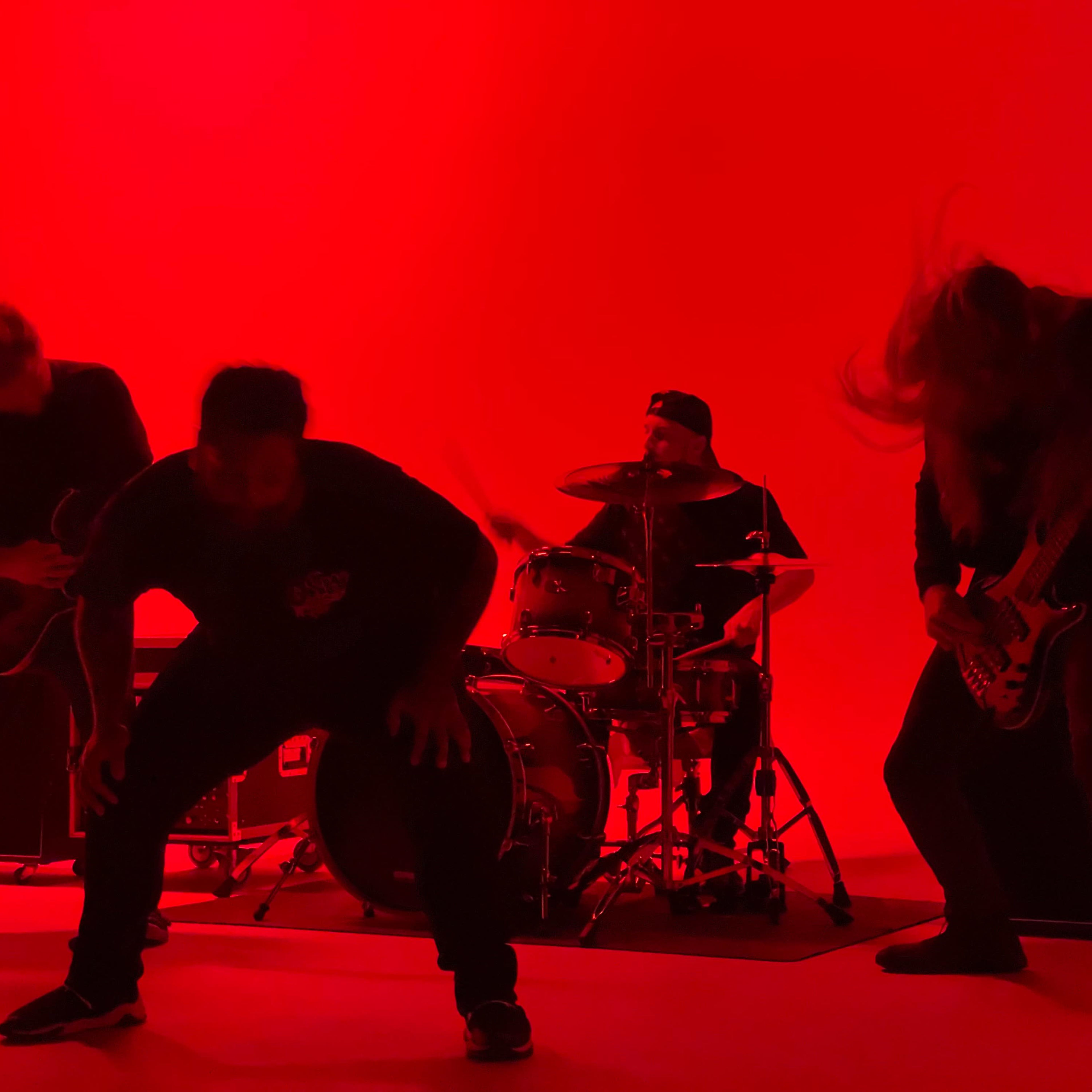 A band performs energetically on stage against a bright red backdrop.
