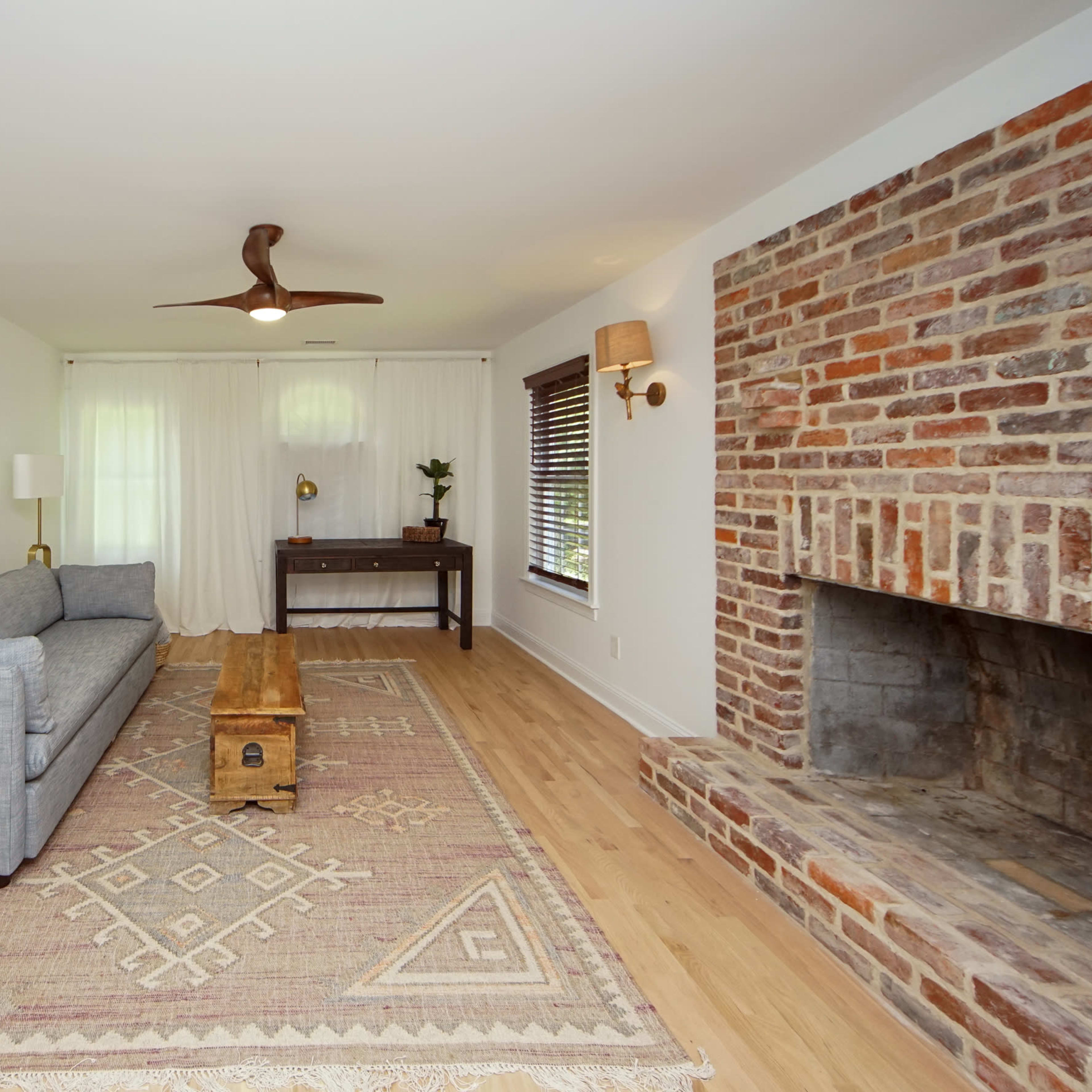 The living room features a gray sofa, a wooden coffee table, a brick fireplace, and a woven basket, all complemented by a large area rug underfoot.