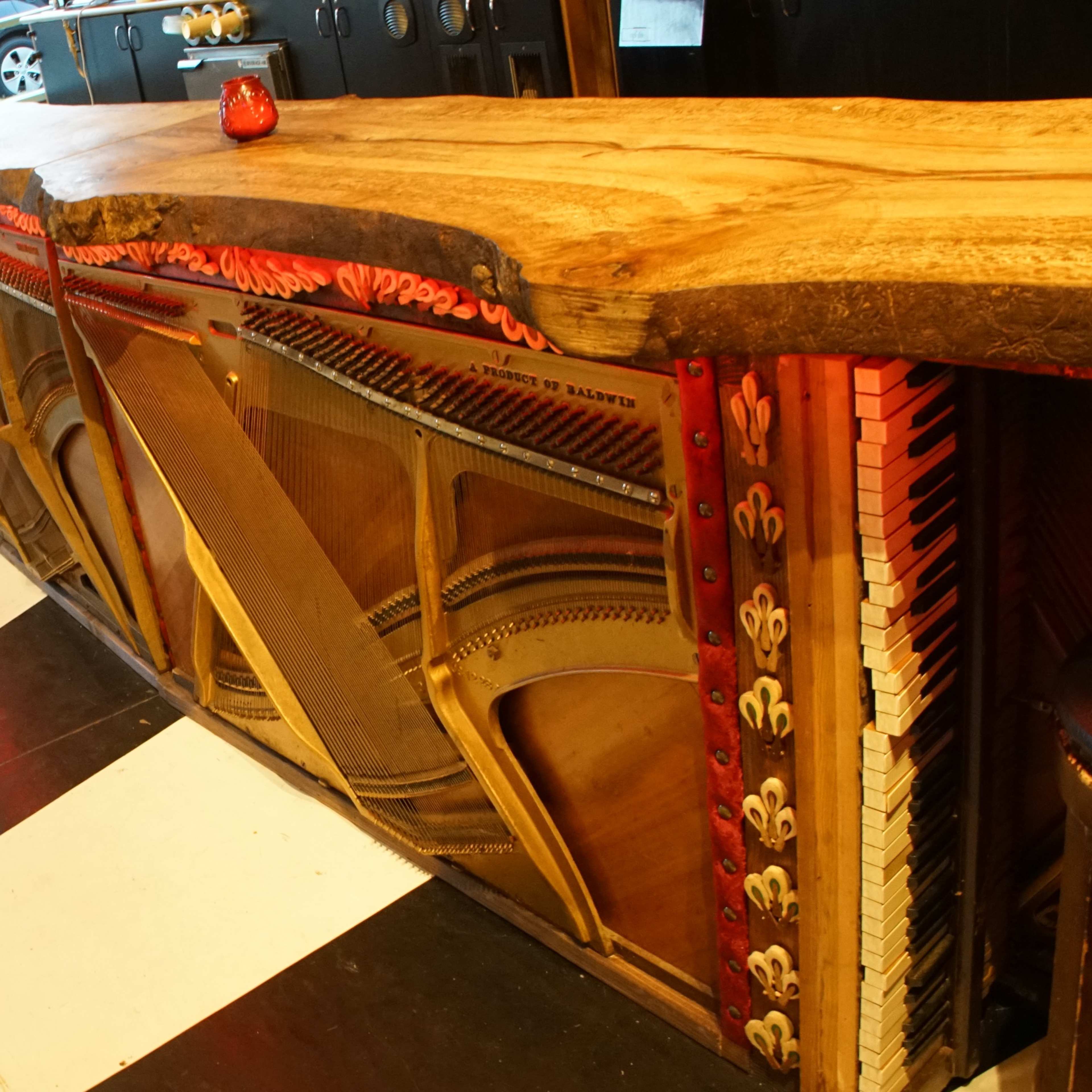 A uniquely designed bar made from a large piece of wood, with a piano integrated into the front, situated on a black and white checked floor.