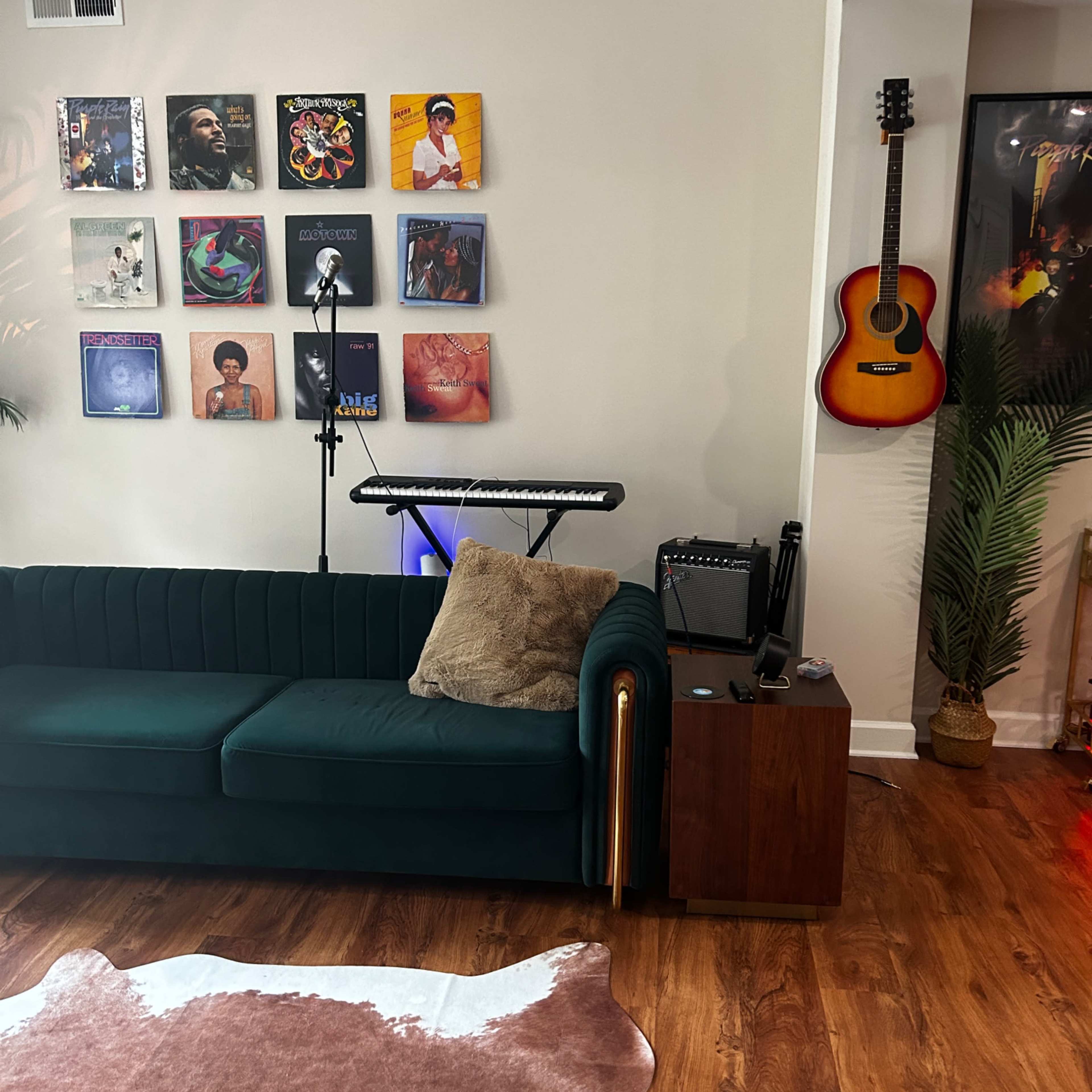 A green sofa is positioned in a room adorned with a wall of vinyl records, a keyboard on a stand, and a guitar hanging nearby.