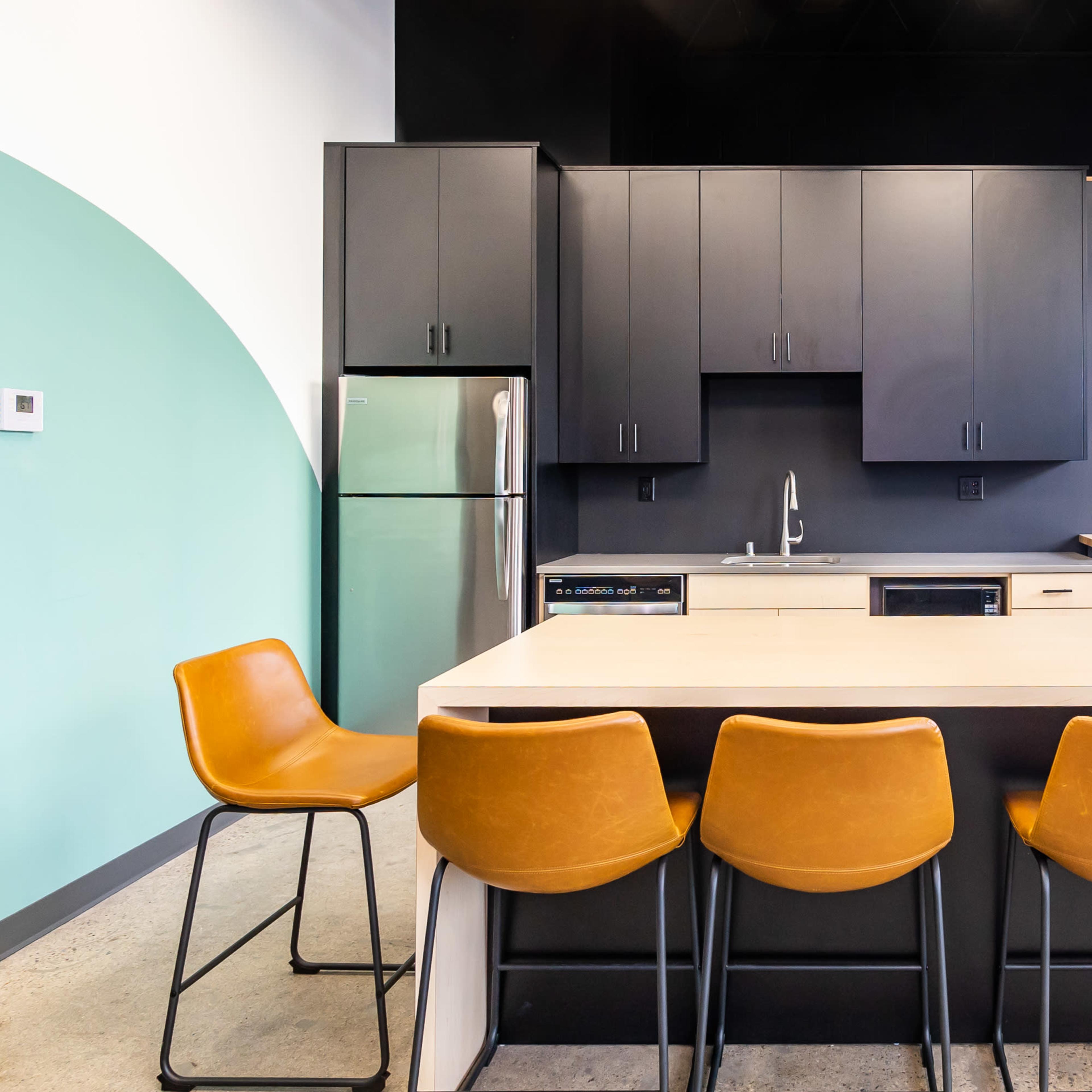 A modern kitchen area with a central island, brown bar stools, black cabinetry, and a television mounted on the wall.