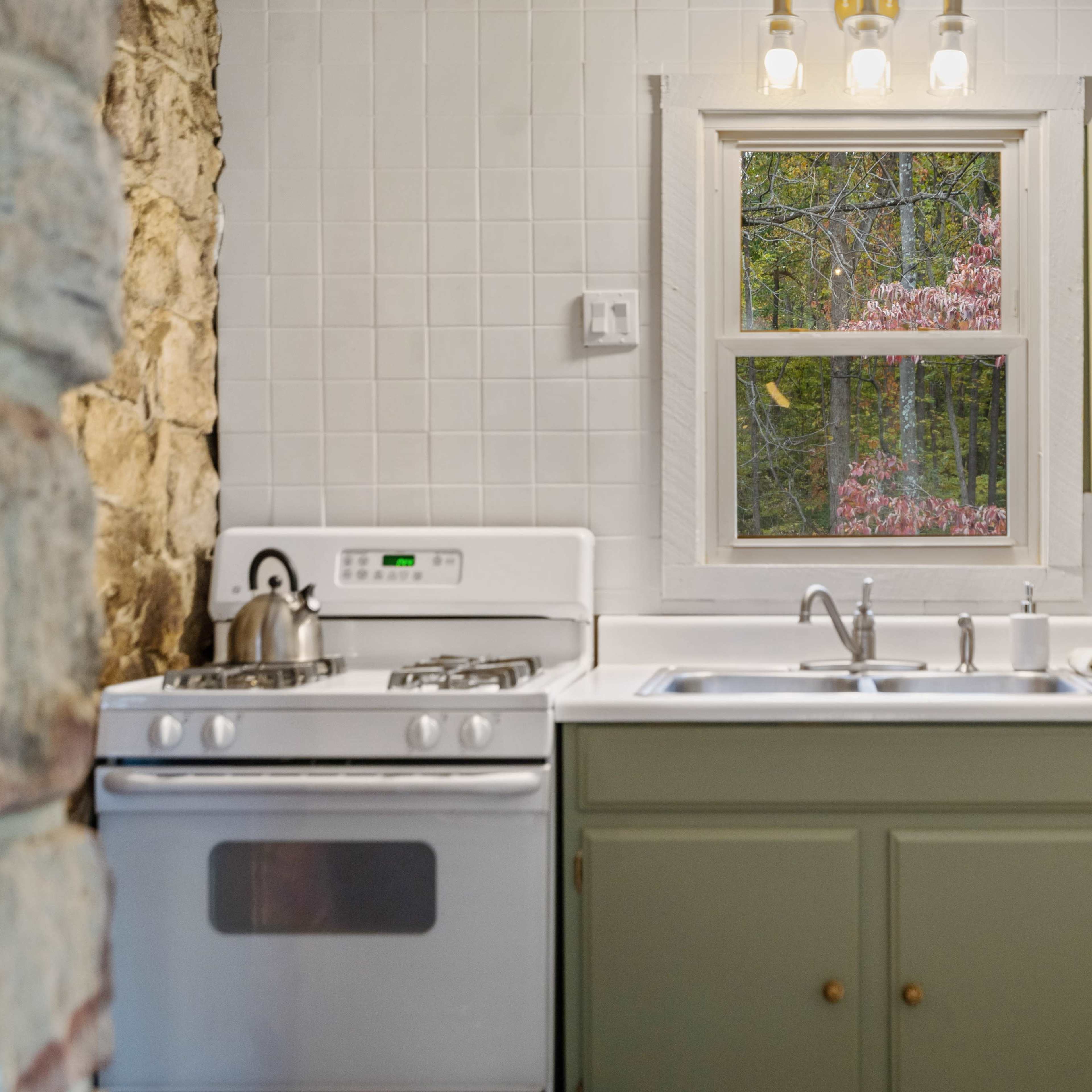 A kitchen features green cabinets, a white stove, and a window revealing a view of trees outside.