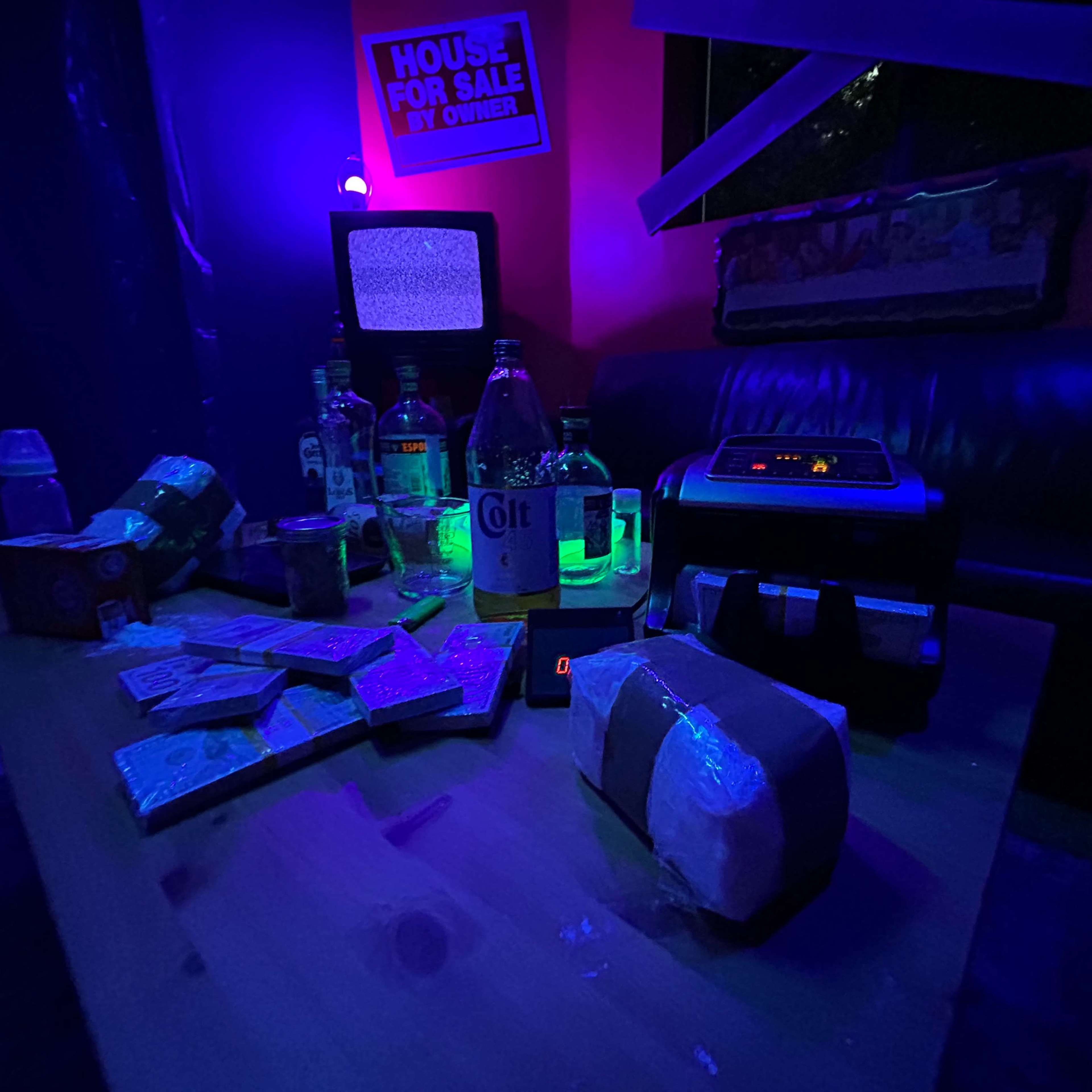 A dimly lit room features a coffee table cluttered with bottles, snacks, and an old clock radio, alongside a vintage television displaying static in the background.