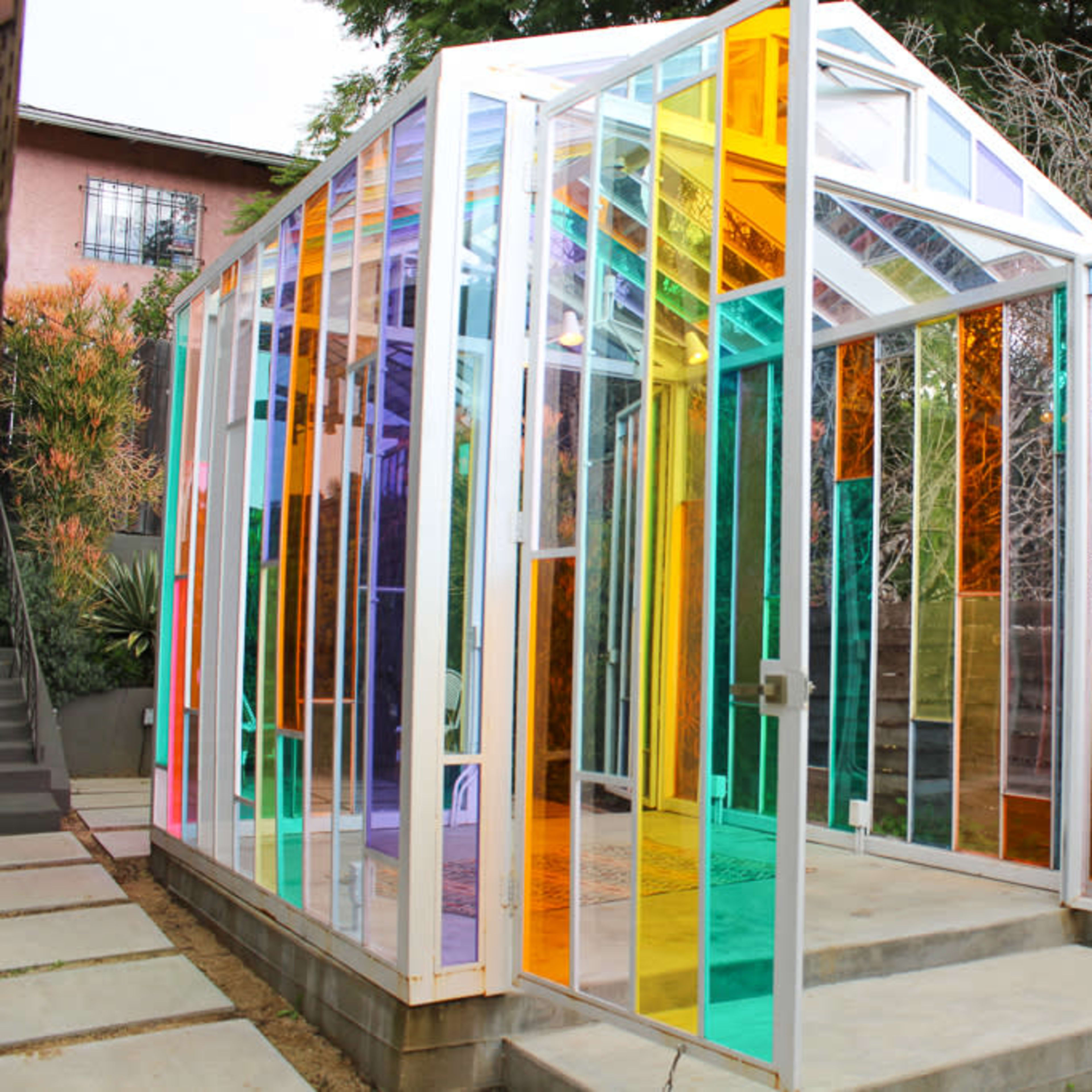 A colorful glass greenhouse surrounded by plants and flowers.